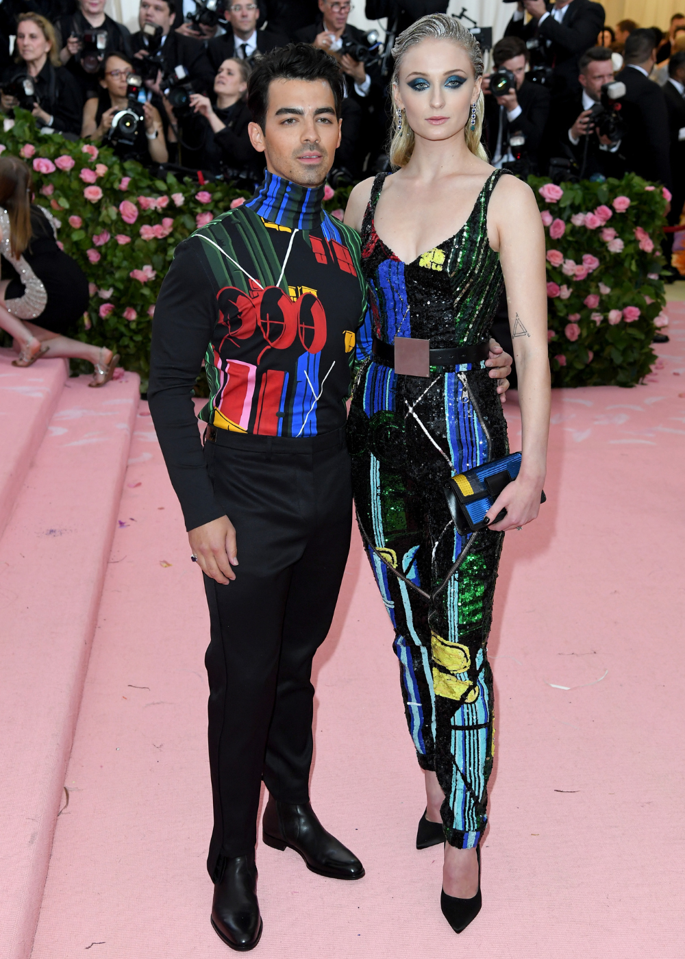 Casal de Hollywood posa junto com looks coordenados em tecidos brilhosos e estampas geométricas coloridas.