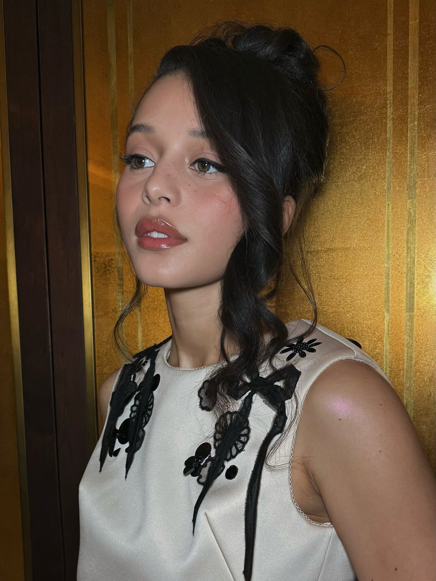 Chase Infiniti posa com vestido off-white em tecido acetinado, bordados pretos delicados e cabelo preso com mechas soltas