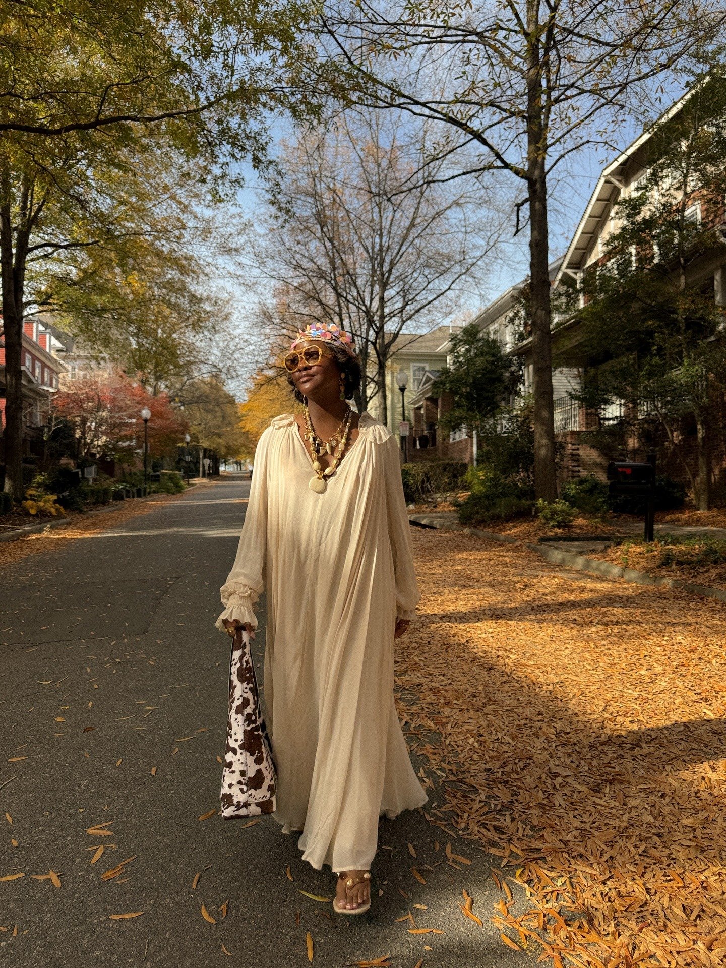 Modelo caminha confiante em vestido longo fluido bege com chinelo de dedo chique dourado, acessórios em tons terrosos