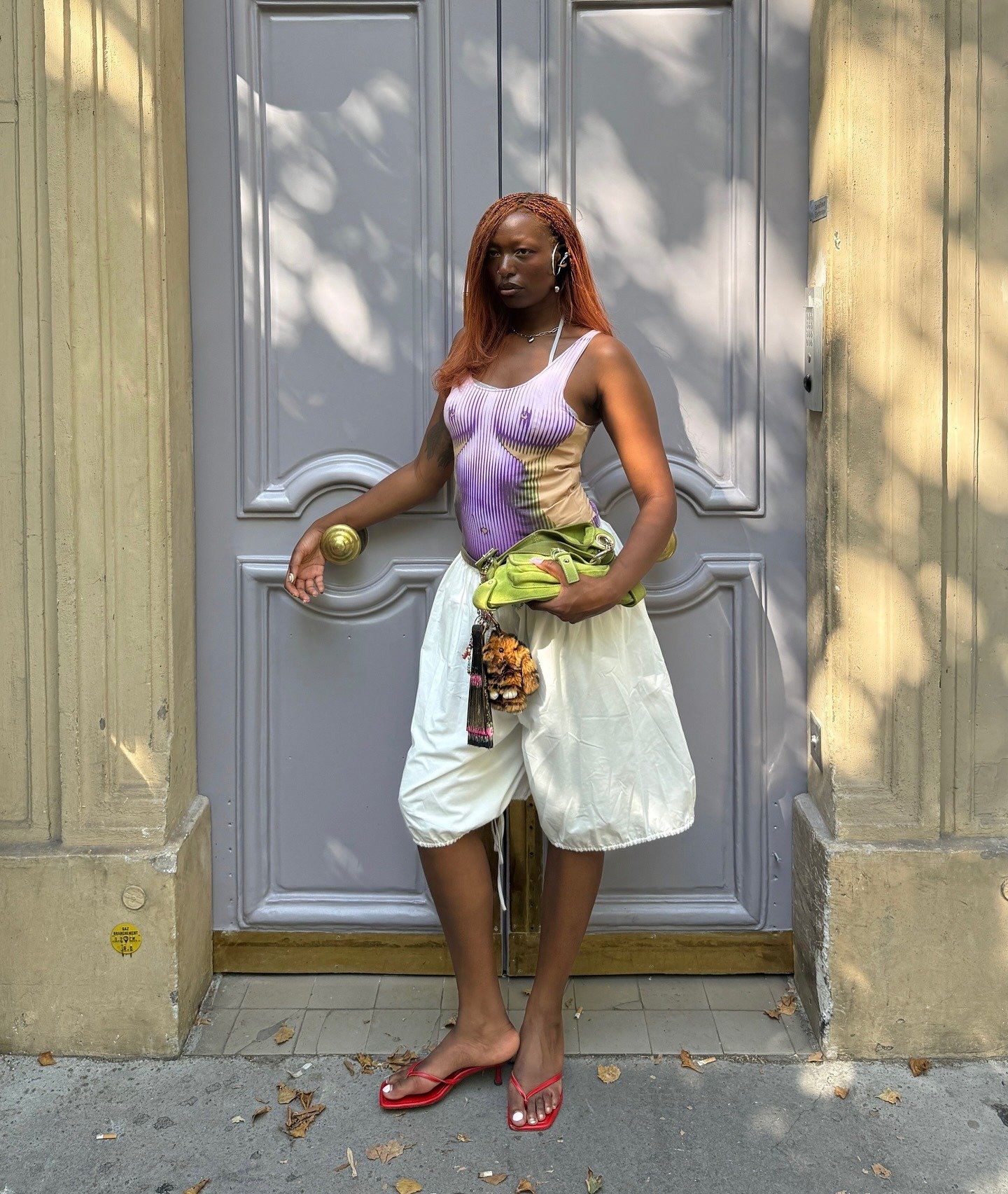 Modelo posa confiante em chinelo de salto alto vermelho com tiras finas, combinando com shorts brancos largos e body lilás