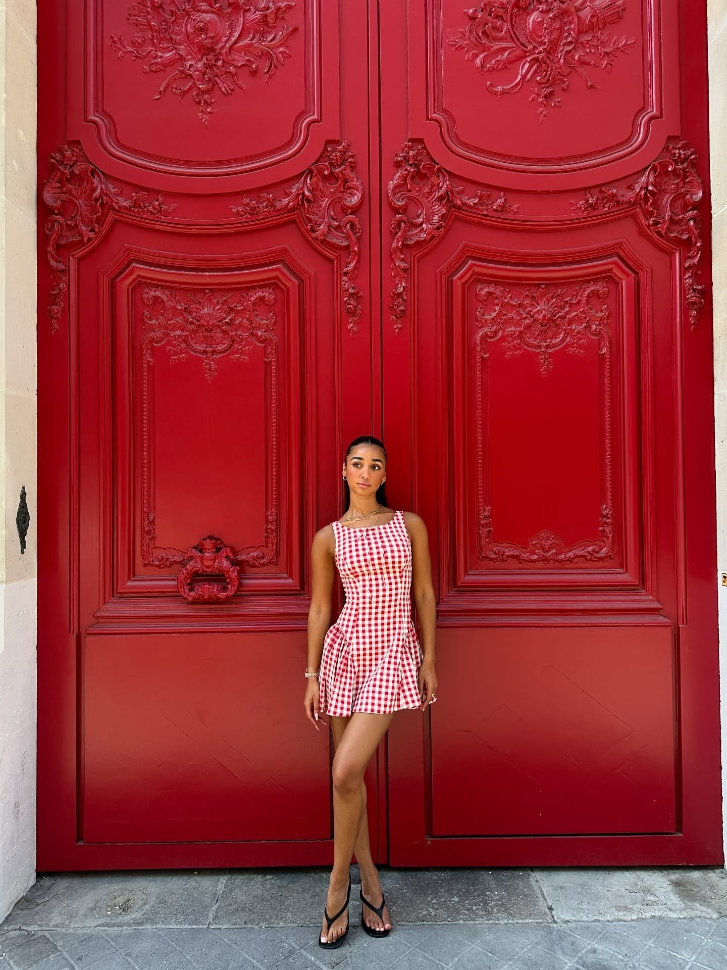 Modelo posa com vestido curto xadrez vermelho e branco de modelagem justa e chinelo de salto alto preto minimalista