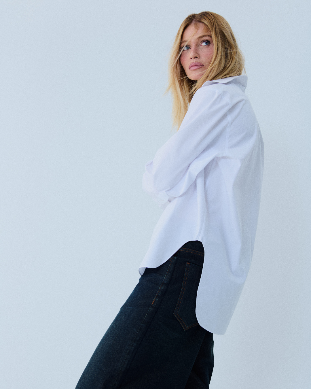 Modelo posa de perfil com camisa branca oversized de algodão e jeans escuro, em campanha de como construir uma marca de moda