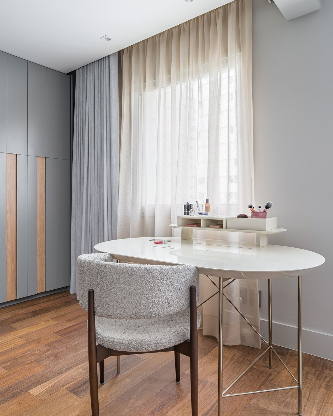 Como organizar o closet com armários cinza e madeira, mesa branca oval, cadeira estofada cinza e ambiente claro que inspira