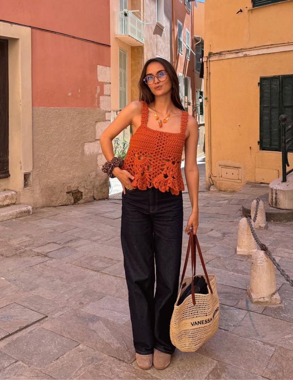 Como usar blusa de crochê: com blusa laranja de crochê, alças largas e barrado floral, combinada com calça preta.