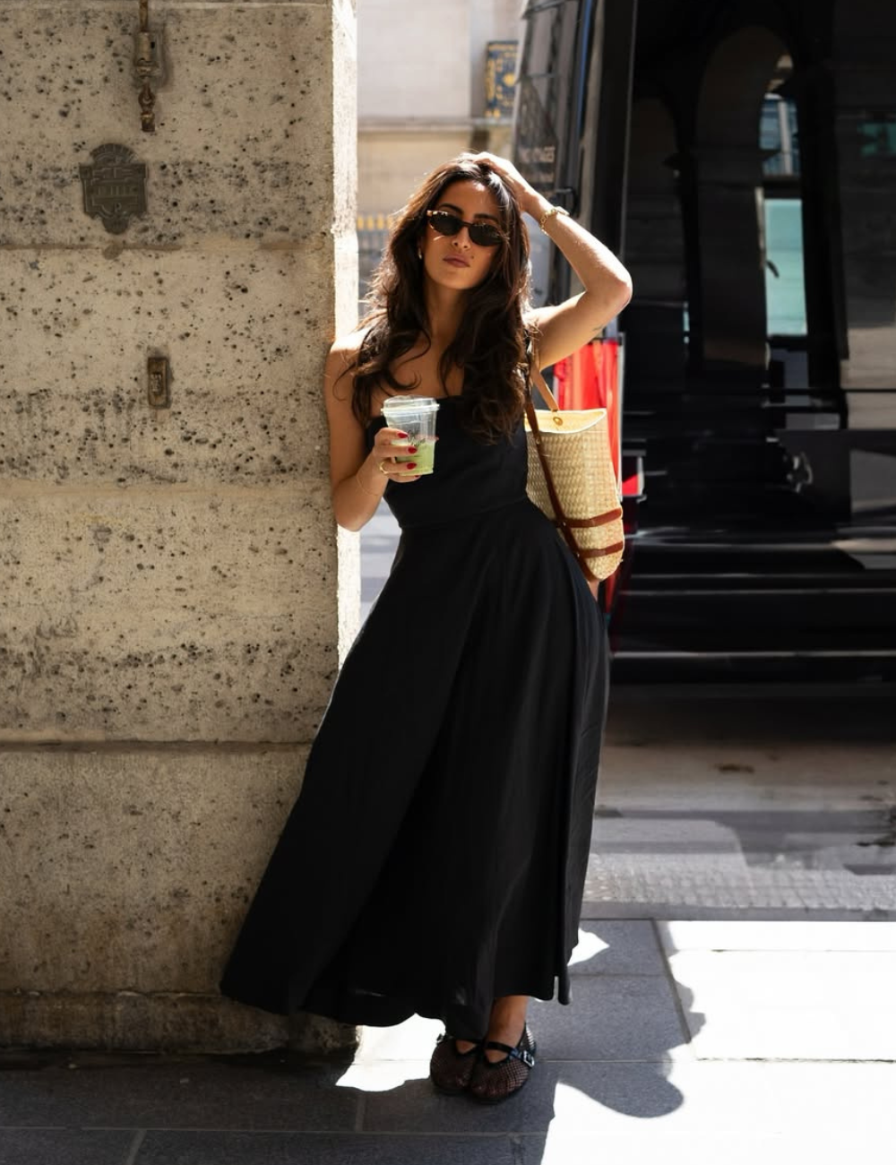 Vestido preto longo de tecido leve, modelagem fluida e alças finas, combinado com bolsa de palha e óculos escuros.