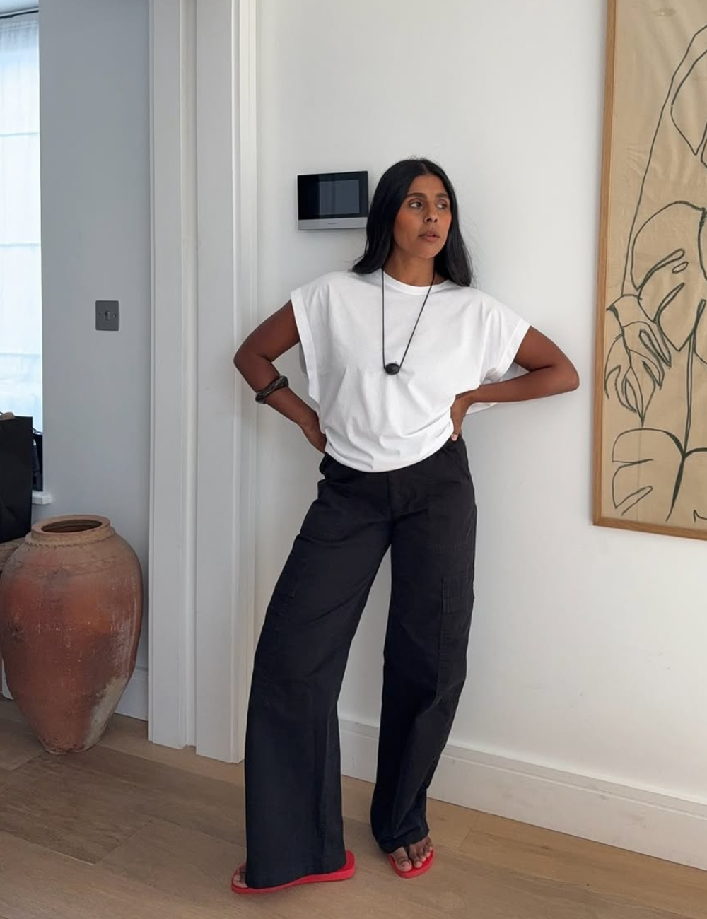 Modelo posa com postura confiante usando calça preta larga de tecido leve e camiseta branca solta.