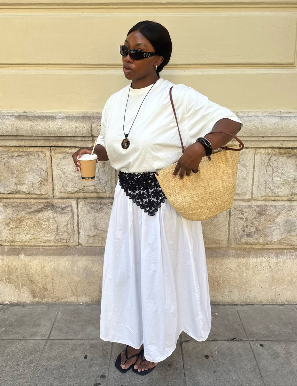 Modelo usa cinto preto de crochê sobre vestido branco fluido de algodão, combinando com chinelos e acessórios pretos.