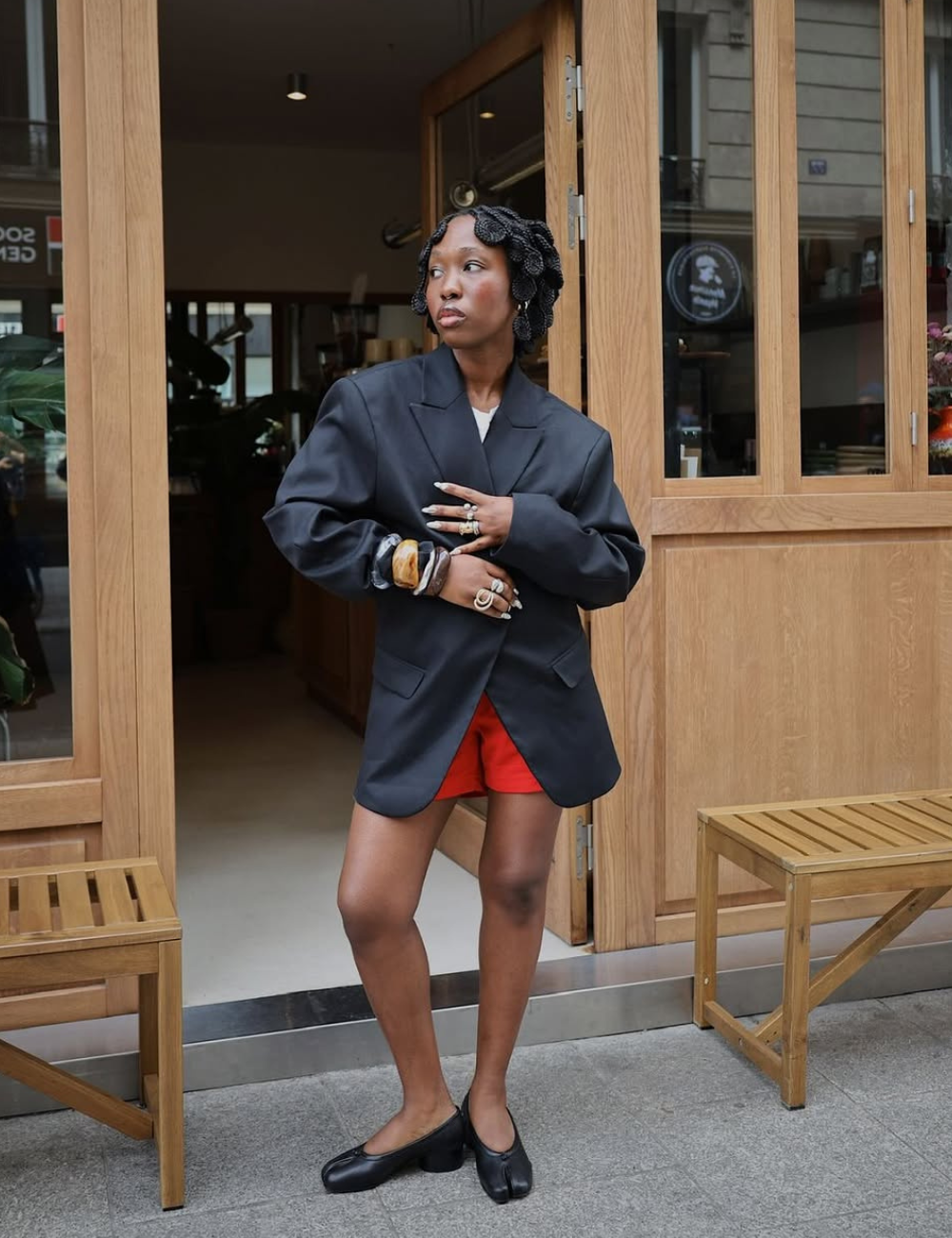 Modelo posa com shorts de alfaiataria vermelho vibrante combinado a blazer oversized preto.