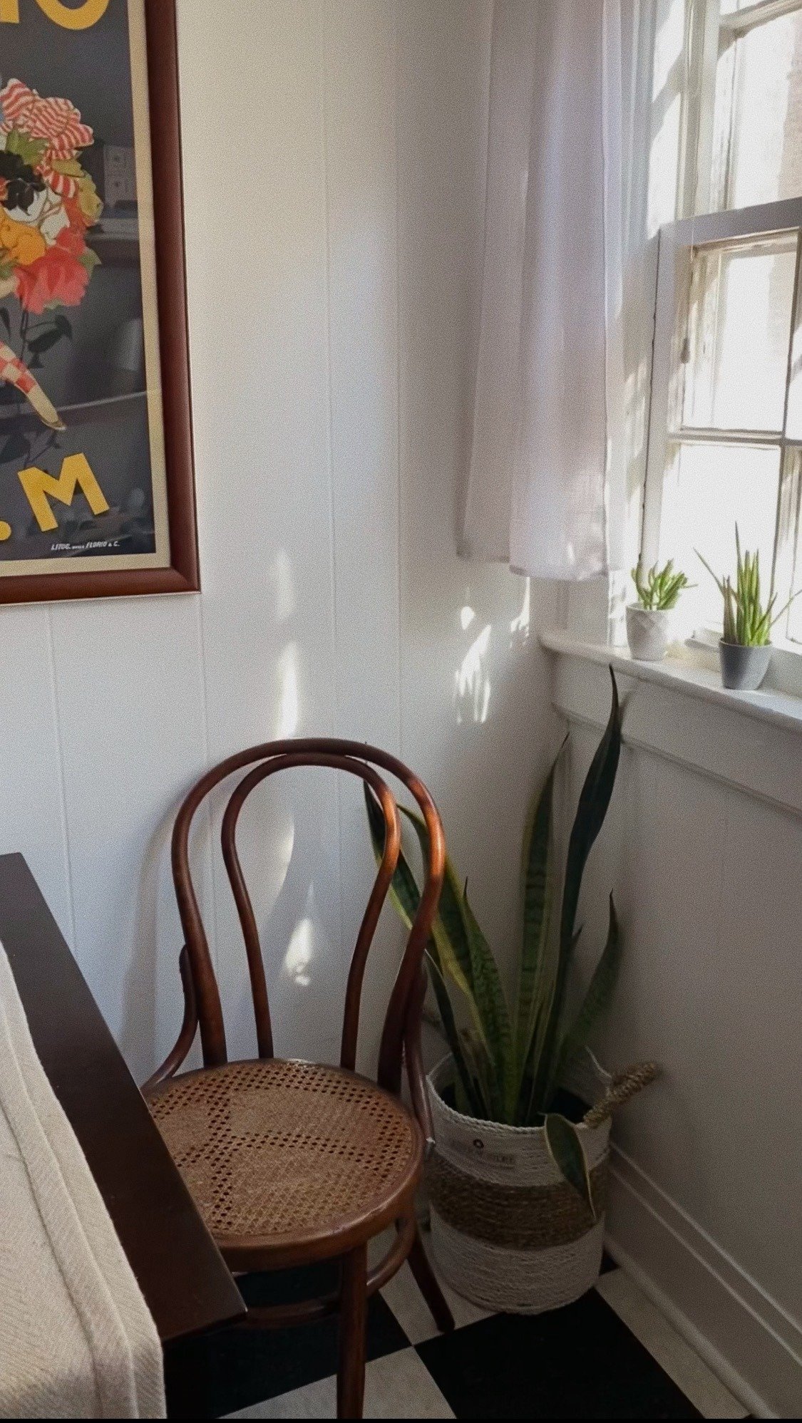 Cozinha retrô com cadeira de madeira curvada e assento de palha, plantas naturais, parede branca e piso xadrez preto e