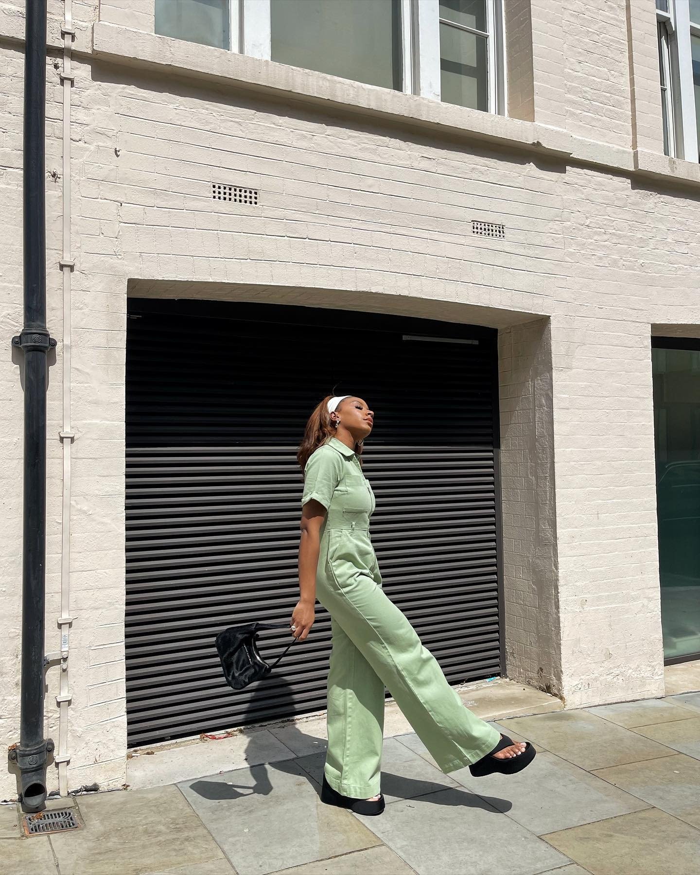 Modelo caminha confiante com macacão verde pastel em tecido estruturado, combinando com acessórios pretos para destacar as