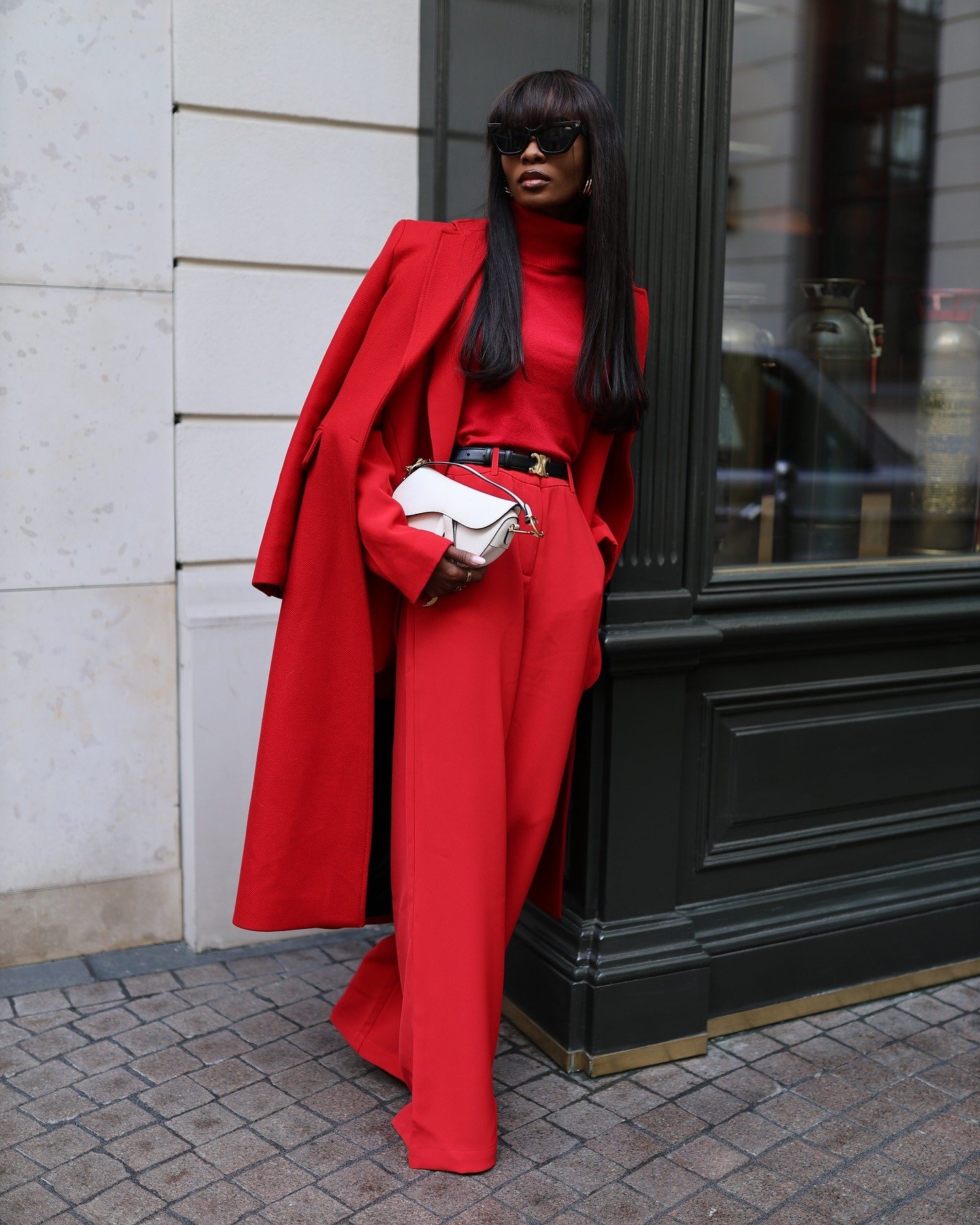 Modelo posa com elegância urbana usando look monocromático em vermelho vibrante, casaco longo, calça ampla e blusa gola