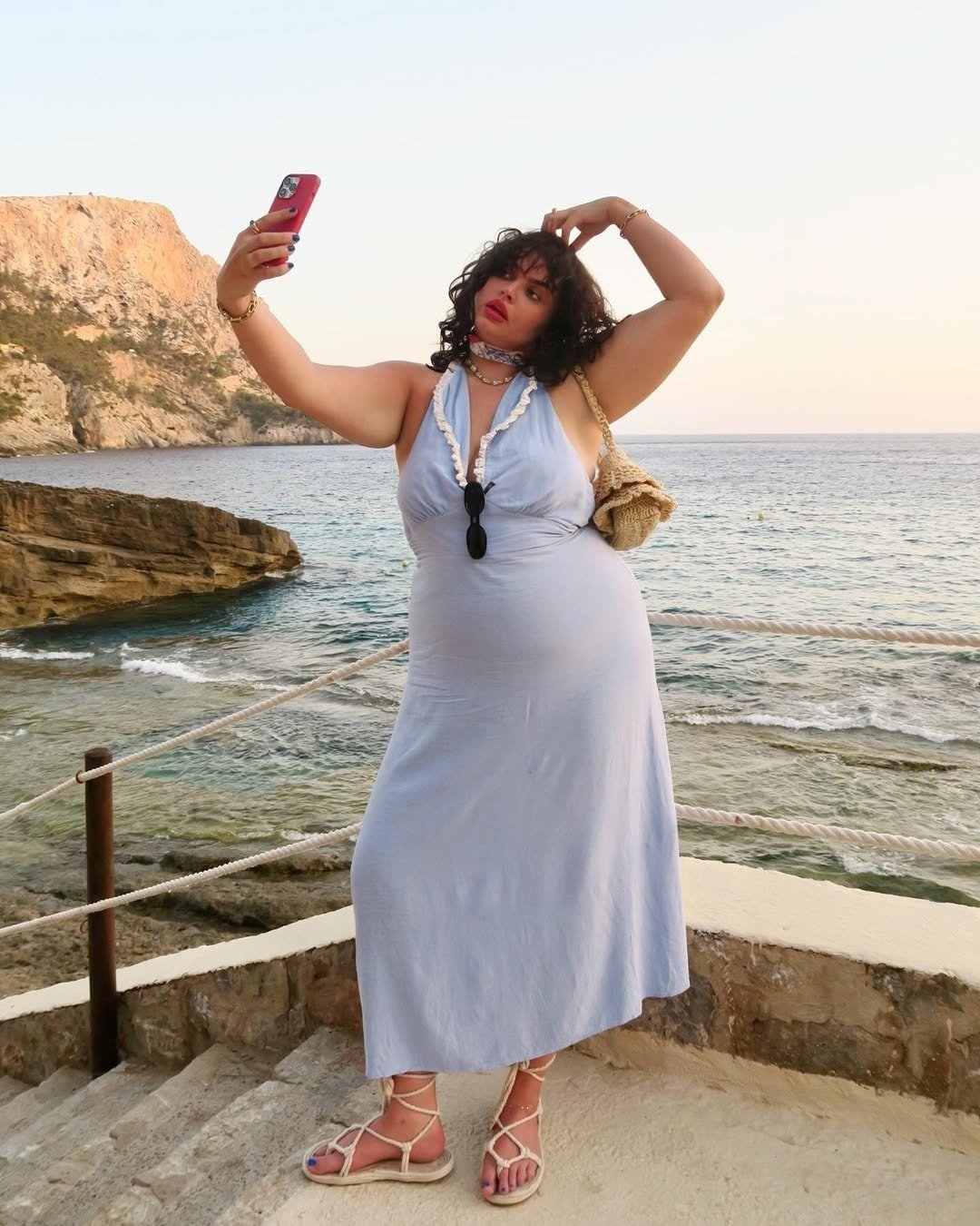 Modelo posa para selfie com vestido azul claro fluido, alças halter e detalhes em babados, refletindo as cores da moda 2026