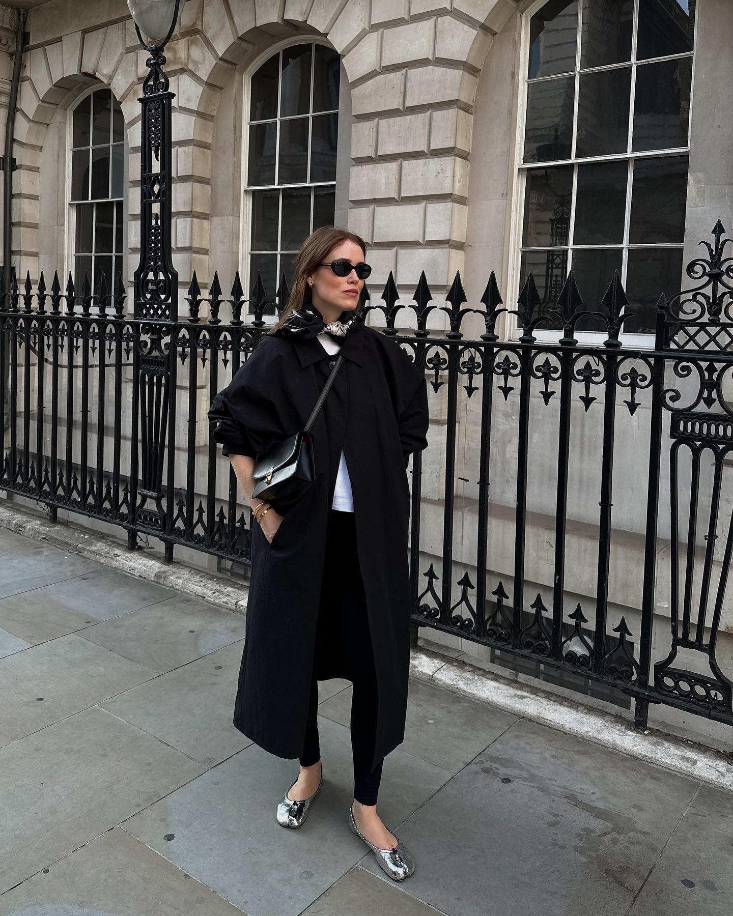 Modelo posa com casaco preto oversized, legging preta e sapatilhas prateadas metalizadas que destacam as cores de sapatilha