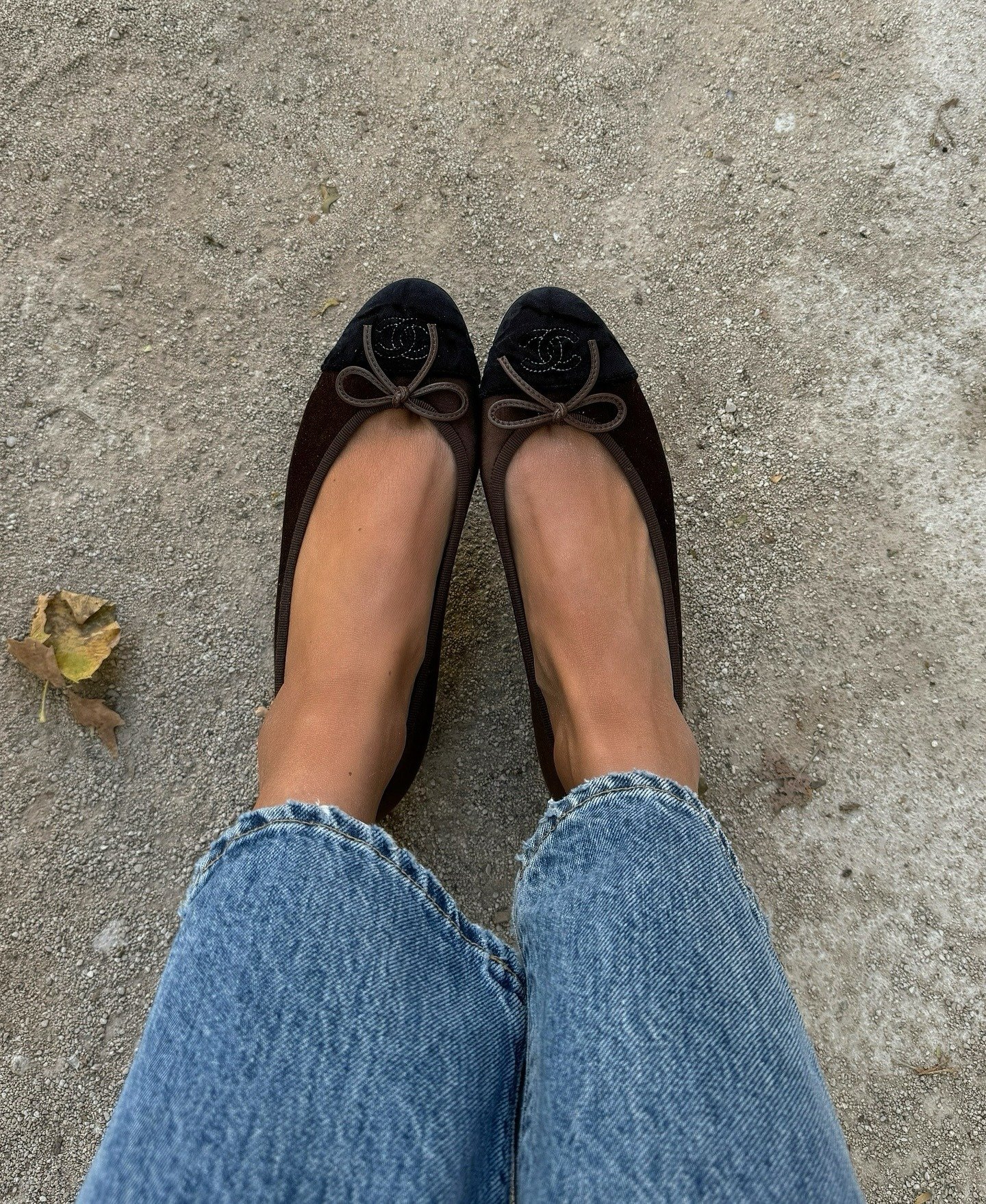 Sapatilhas clássicas em camurça marrom com bico preto e laço frontal, combinando conforto e elegância casual com jeans azul.