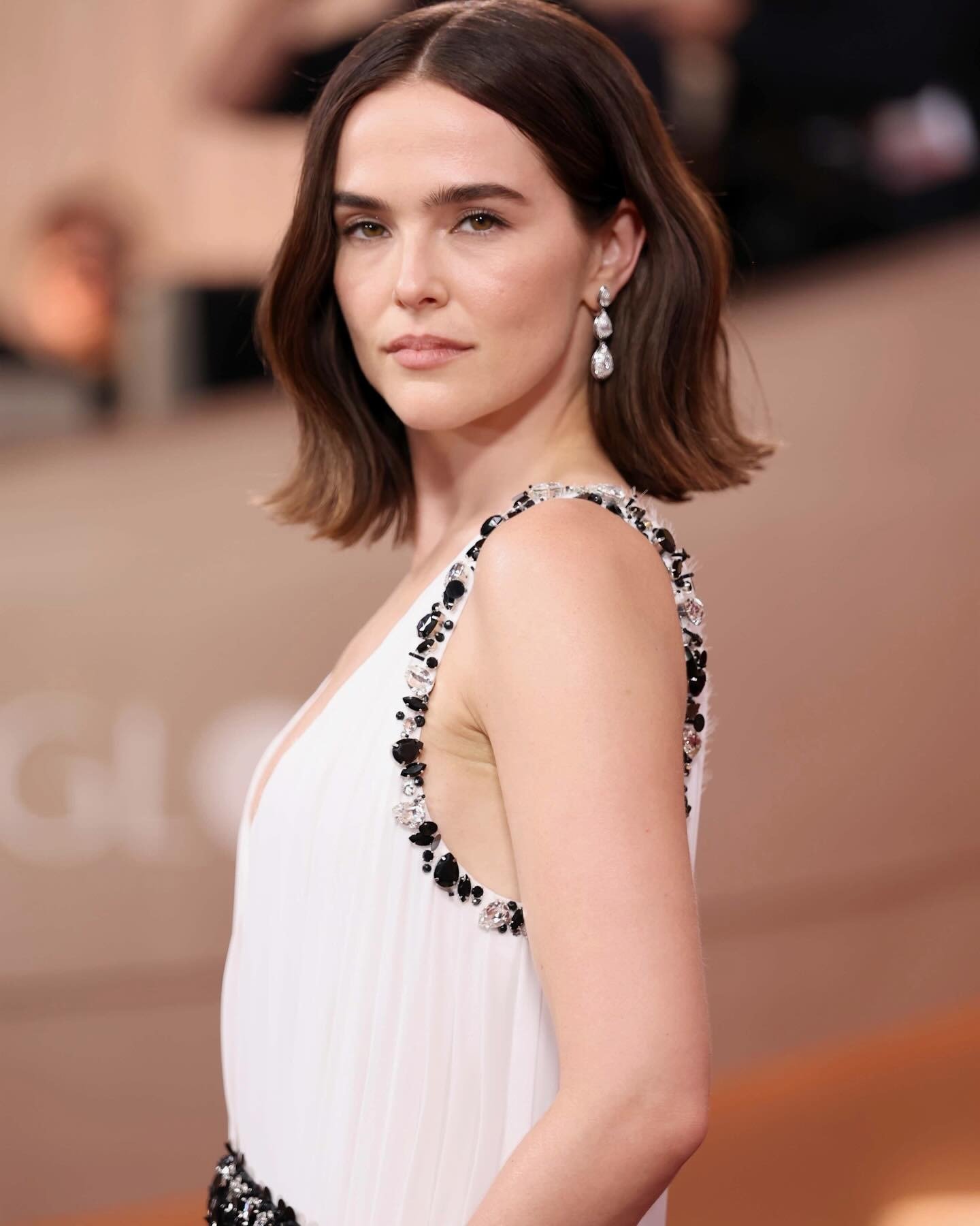 Modelo posa com cabelo curtinho castanho em corte reto, vestido branco com bordados pretos e cristais, expressão serena e