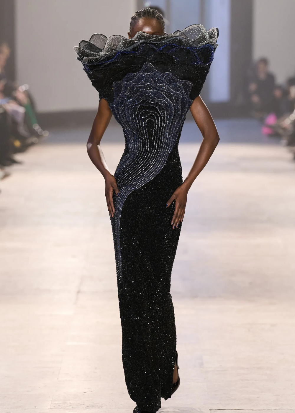 Modelo caminha com vestido longo justo de alta-costura primavera 2026 em preto brilhante, gola estruturada e bordados