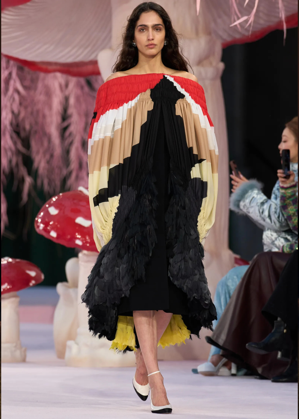 Modelo posa com vestido ombro a ombro em alta-costura primavera 2026, combinando plissados, penas e cores vibrantes como