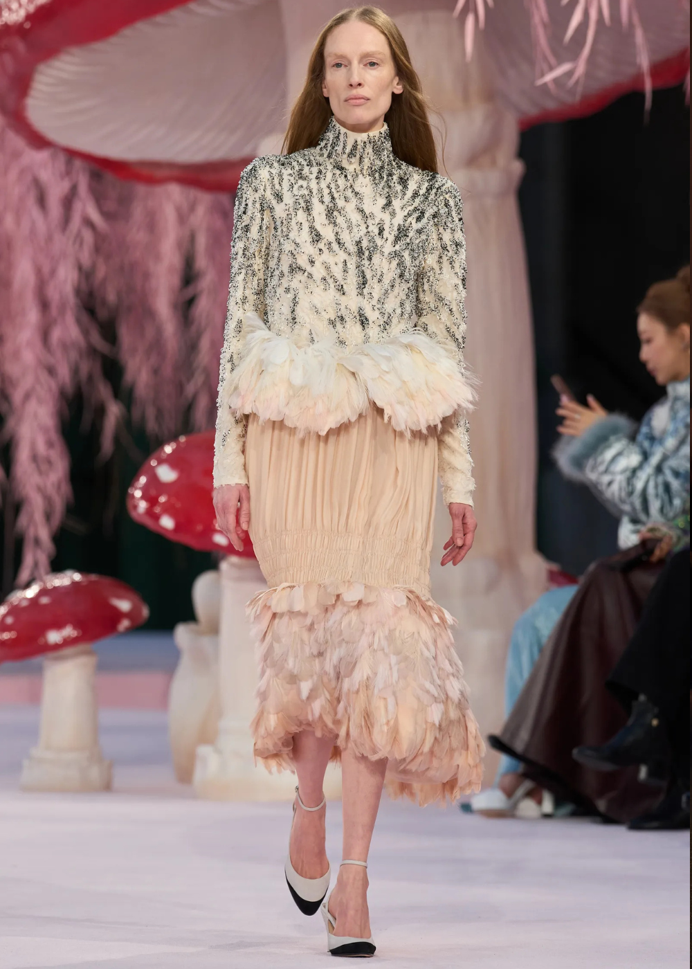 Modelo caminha com postura confiante usando vestido de alta-costura primavera 2026 em tons neutros, com texturas de plumas e