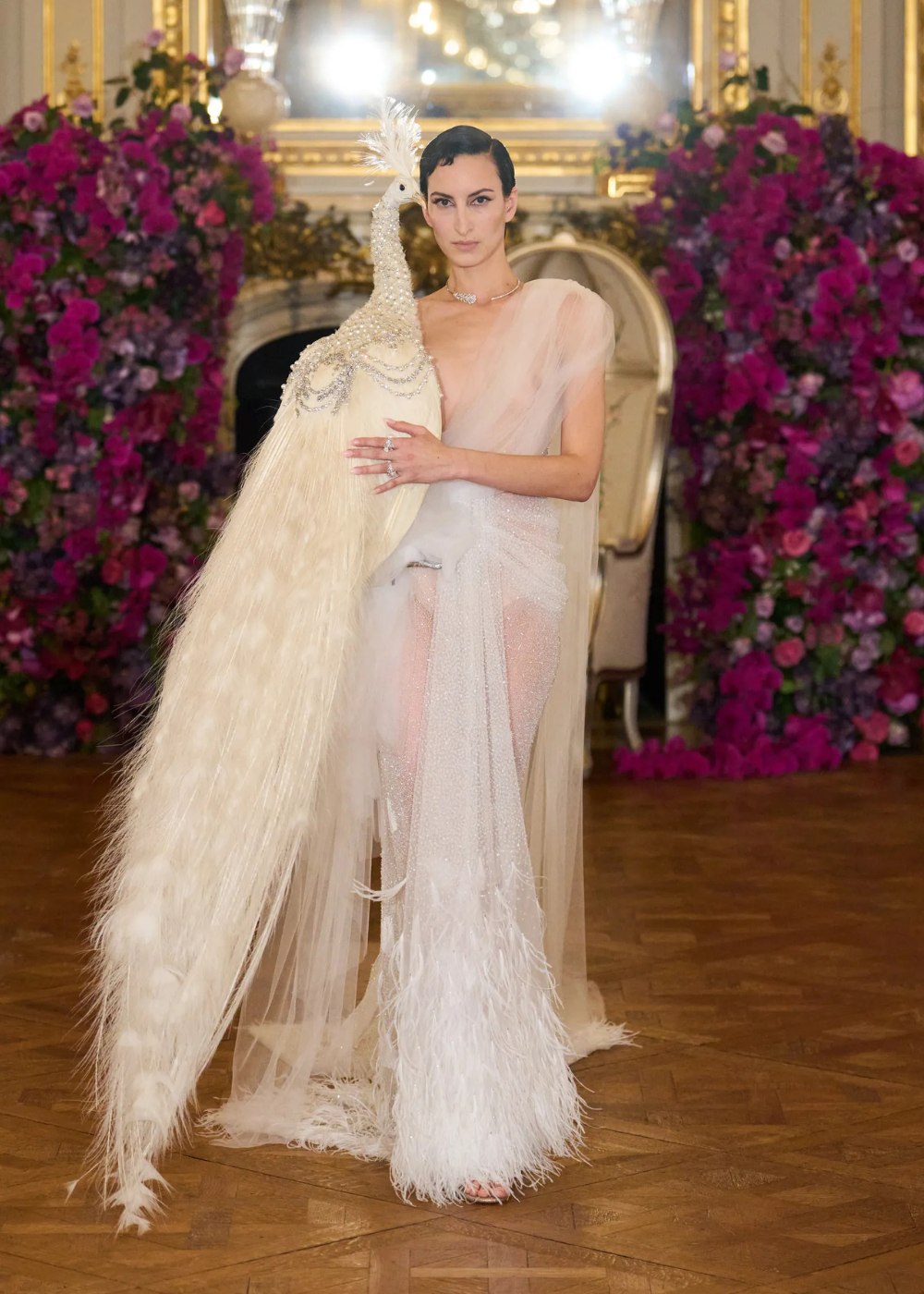 Modelo posa com vestido de tule nude e transparência, detalhes em plumas e bordados, refletindo as tendências da temporada