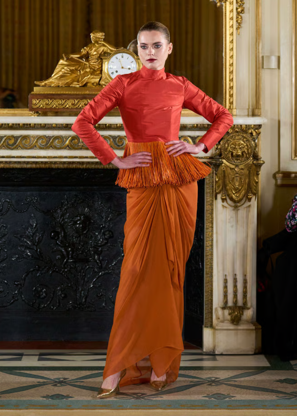 Modelo posa com postura confiante usando alta-costura primavera 2026 em tons quentes, blusa estruturada com franjas e saia