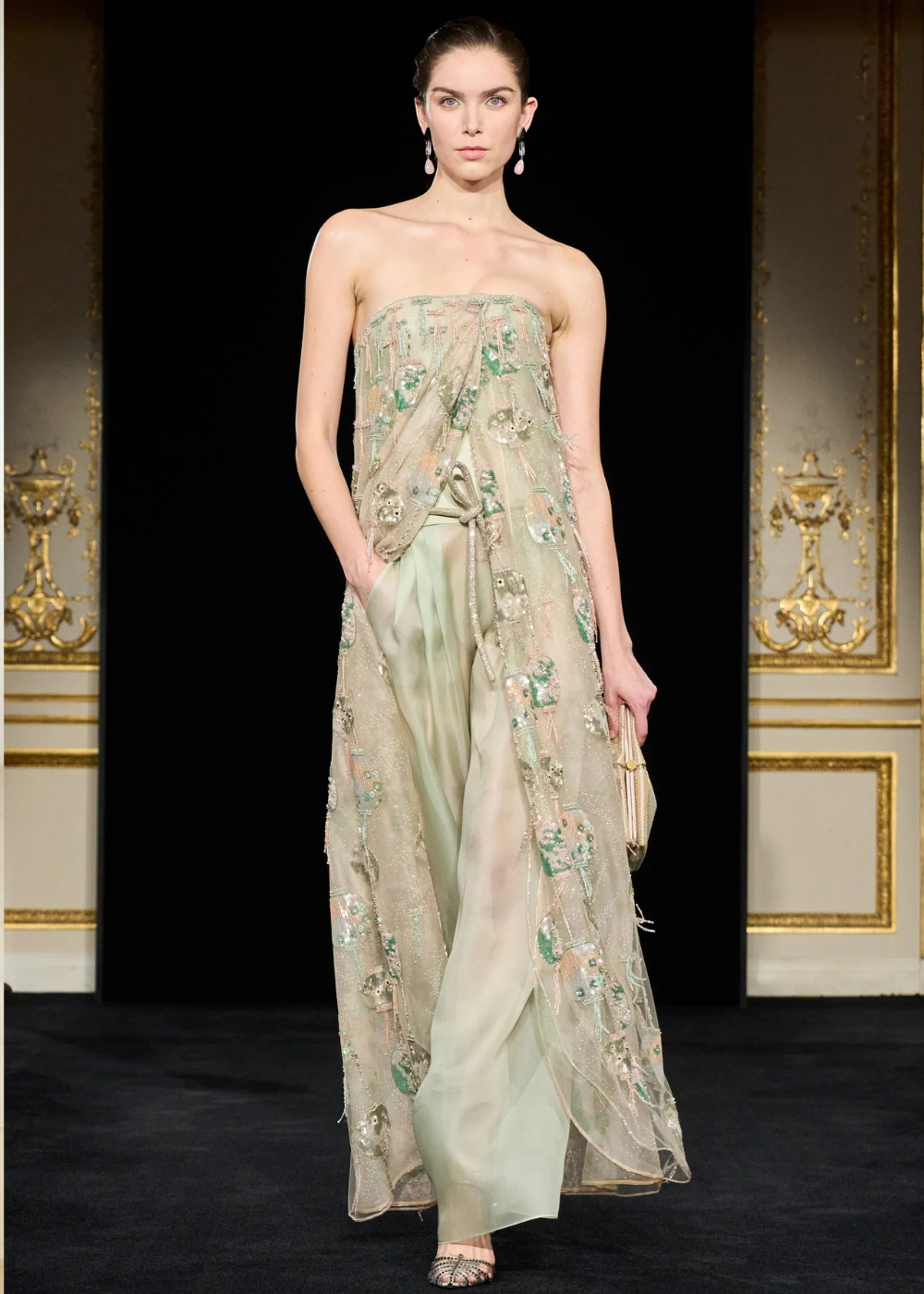 Modelo posa com vestido tomara que caia em tule bordado translúcido sobre calça fluida verde pastel, expressando delicadeza