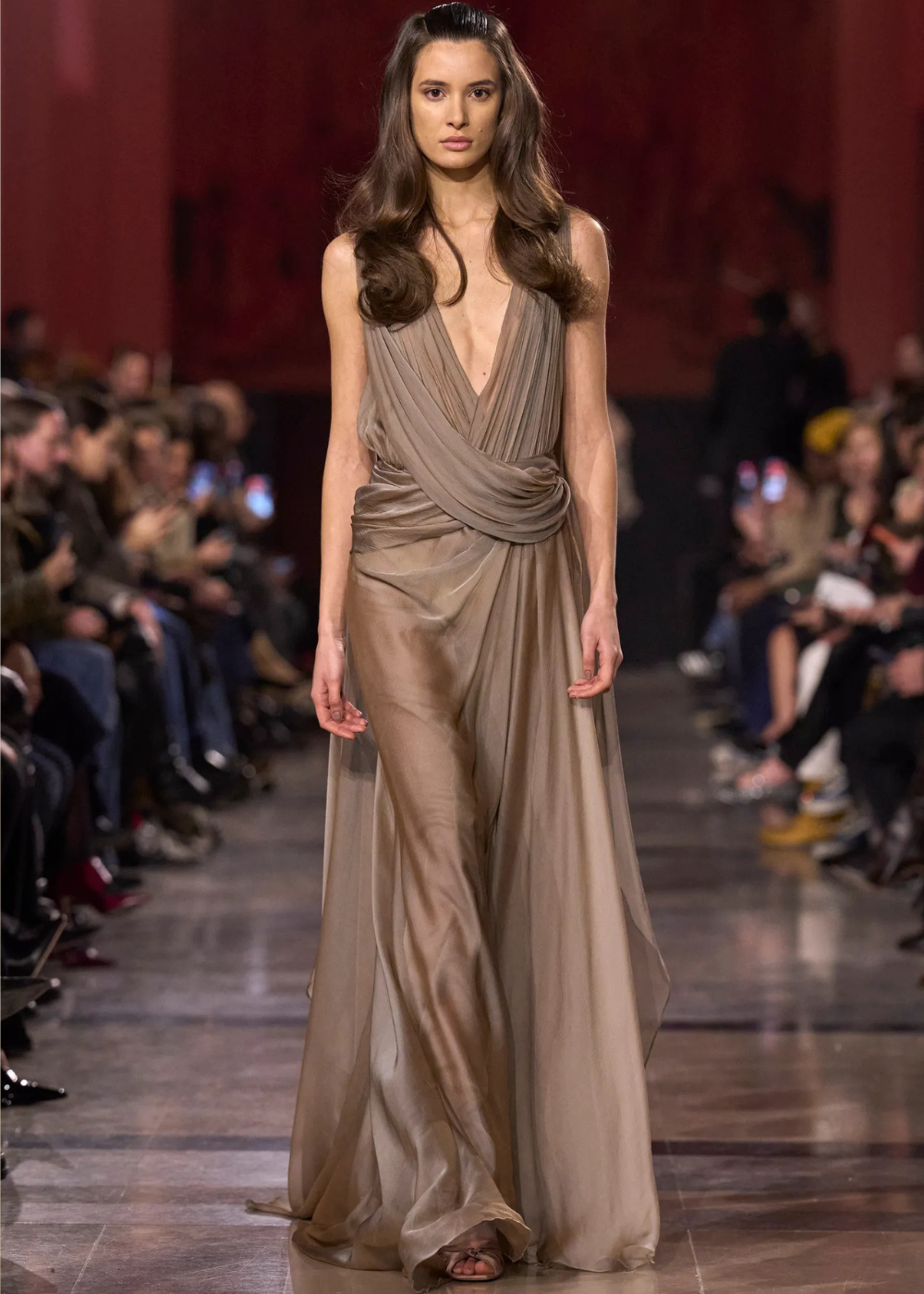 Modelo caminha com vestido fluido de alta-costura primavera 2026 em tom neutro, com drapeados e decote profundo, destacando