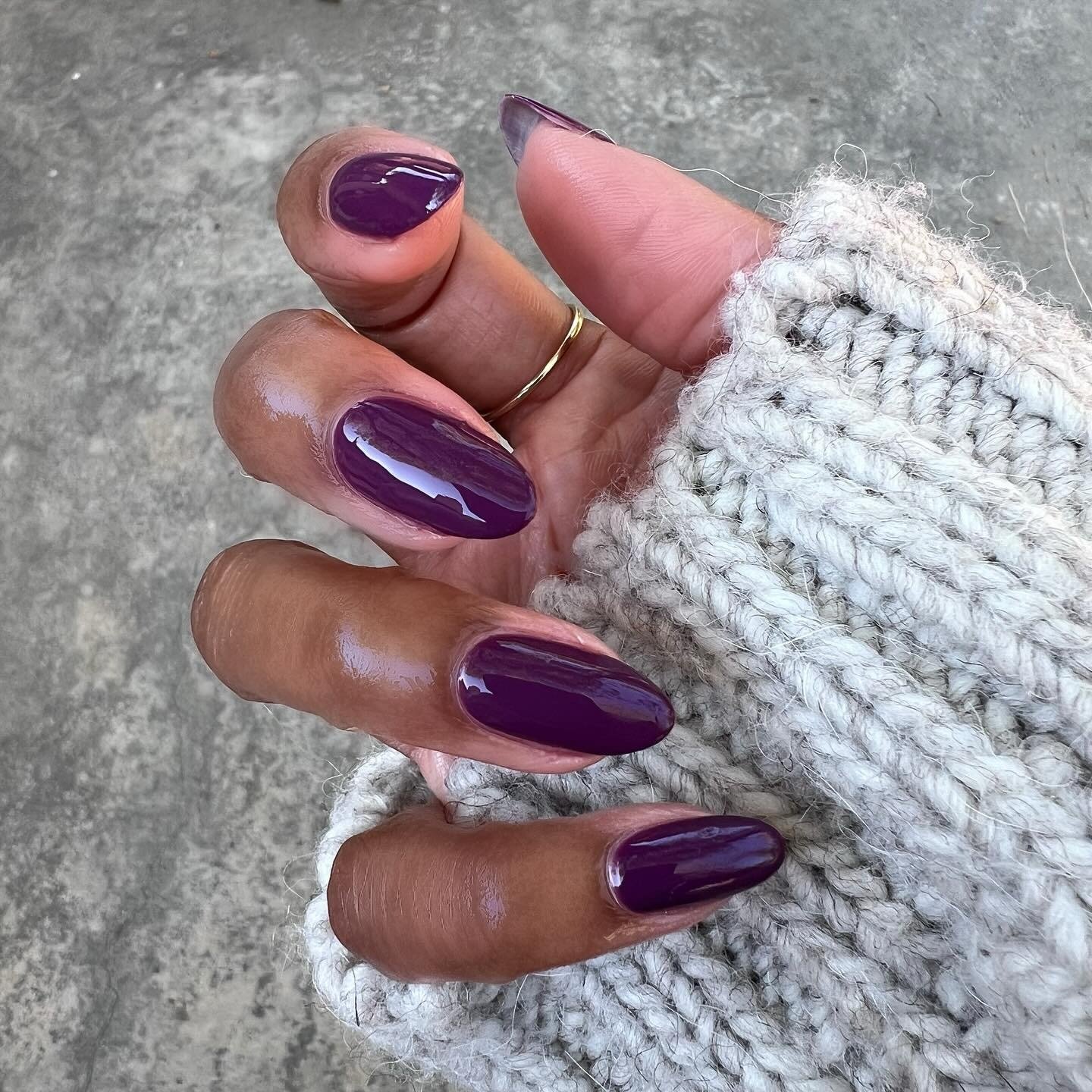 Mãos com esmaltes em alta roxo brilhoso e unhas ovaladas combinam com suéter de tricô cinza, criando estilo aconchegante e