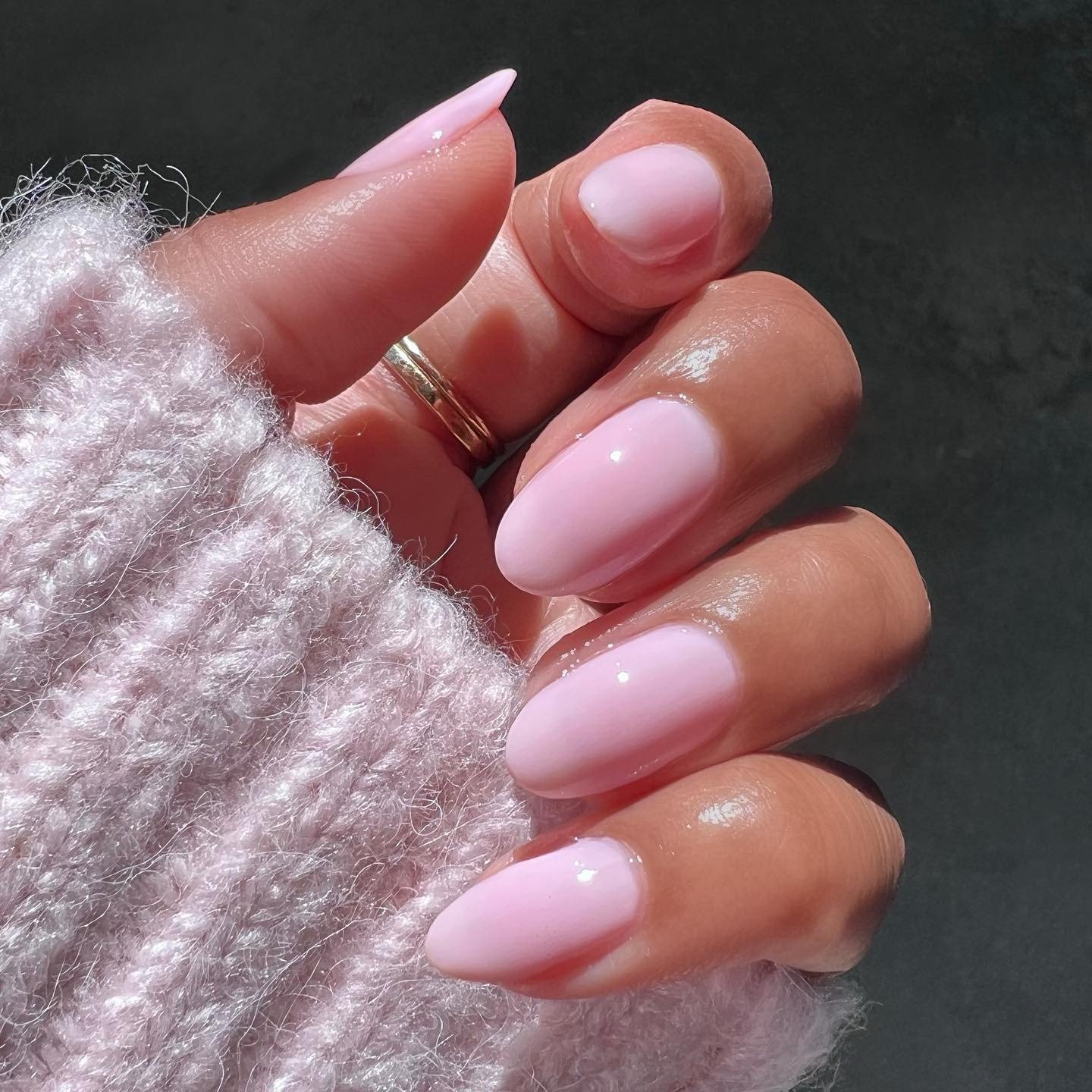 Unhas longas em formato amendoado com esmaltes em alta na cor rosa claro, combinando com suéter felpudo rosa, em luz natural.
