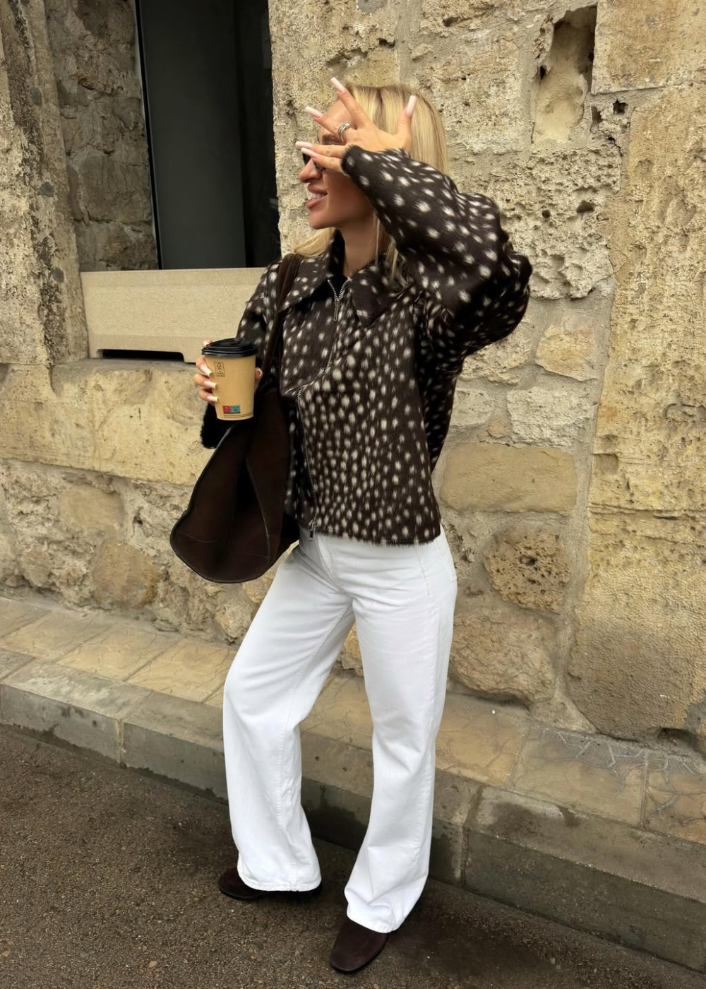 Modelo posa sorrindo e protegendo o rosto com a mão, veste jaqueta de tecido felpudo com estampa de cervo em tons de marrom.