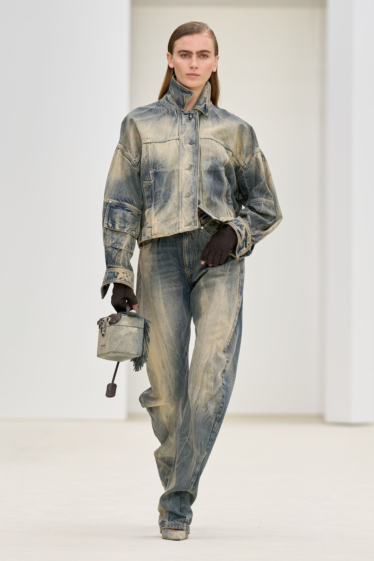 Modelo caminha com postura confiante usando calça barrel jeans de lavagem estonada, combinada com jaqueta oversized e luvas