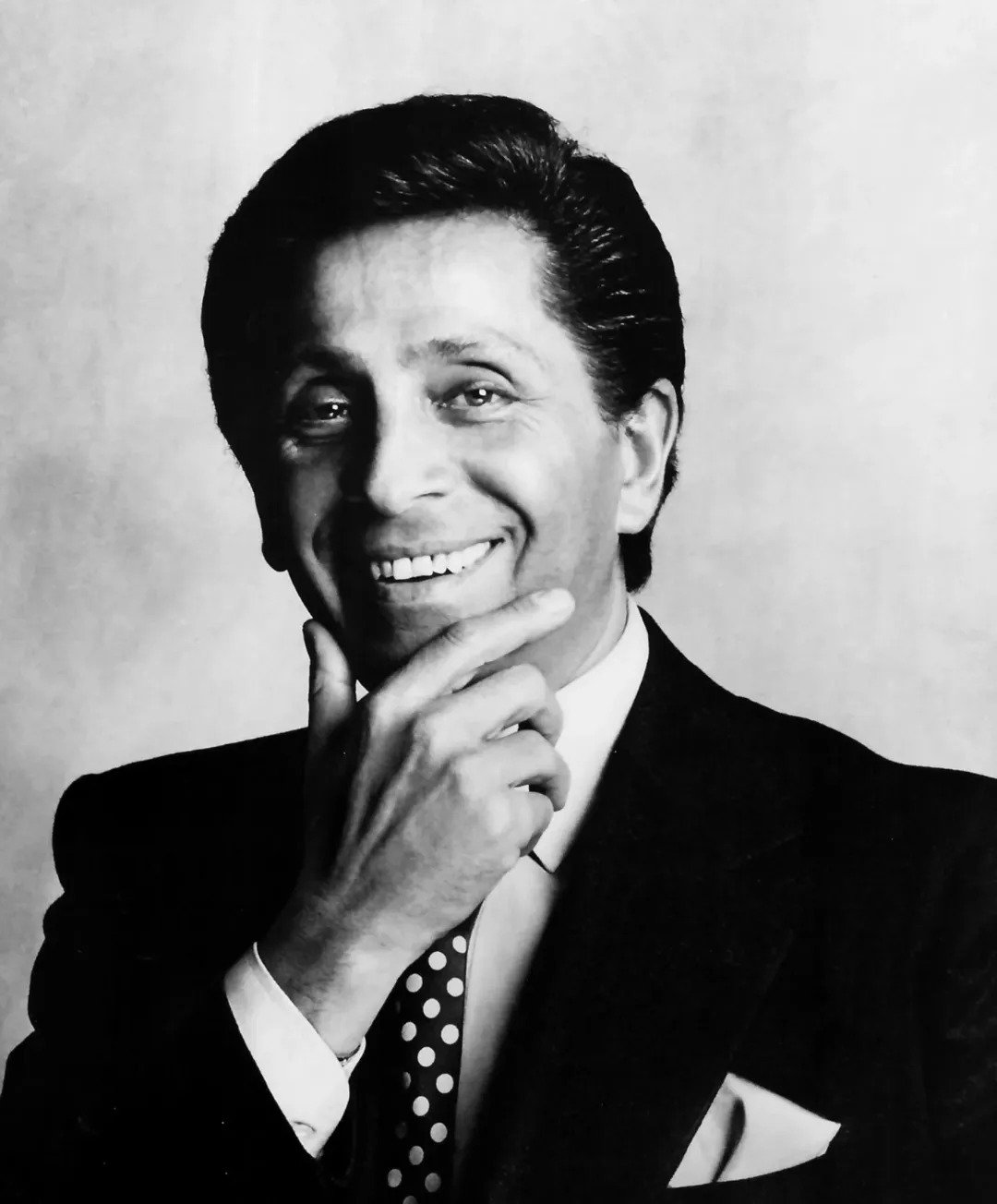 Retrato em preto e branco de homem sorridente com terno escuro, camisa branca e gravata de bolinhas, postura confiante e