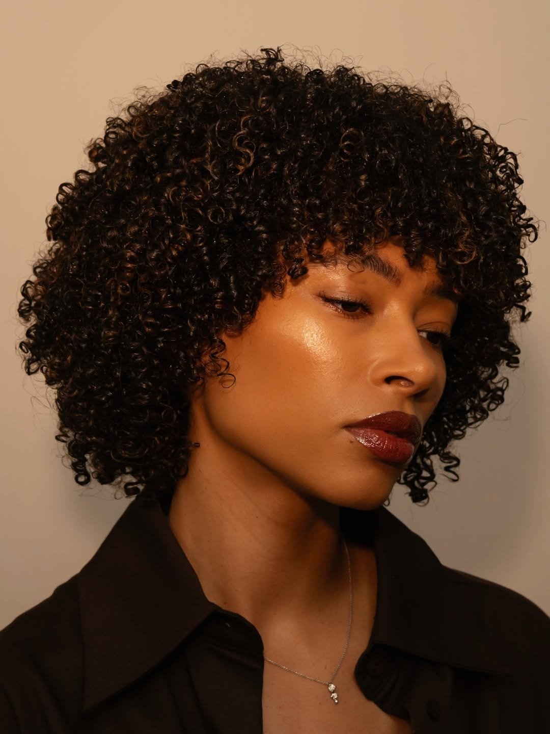 Modelo com cabelo cacheado volumoso e saudável, pele iluminada, batom vinho, óleos essenciais para queda de cabelo