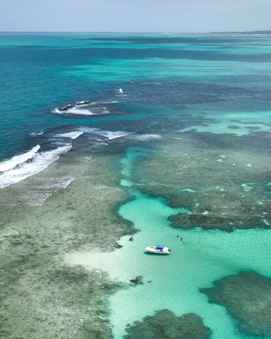 Mar azul-turquesa e verde água com barco branco e azul em mar raso, cenário ideal para o guia do verão brasileiro.