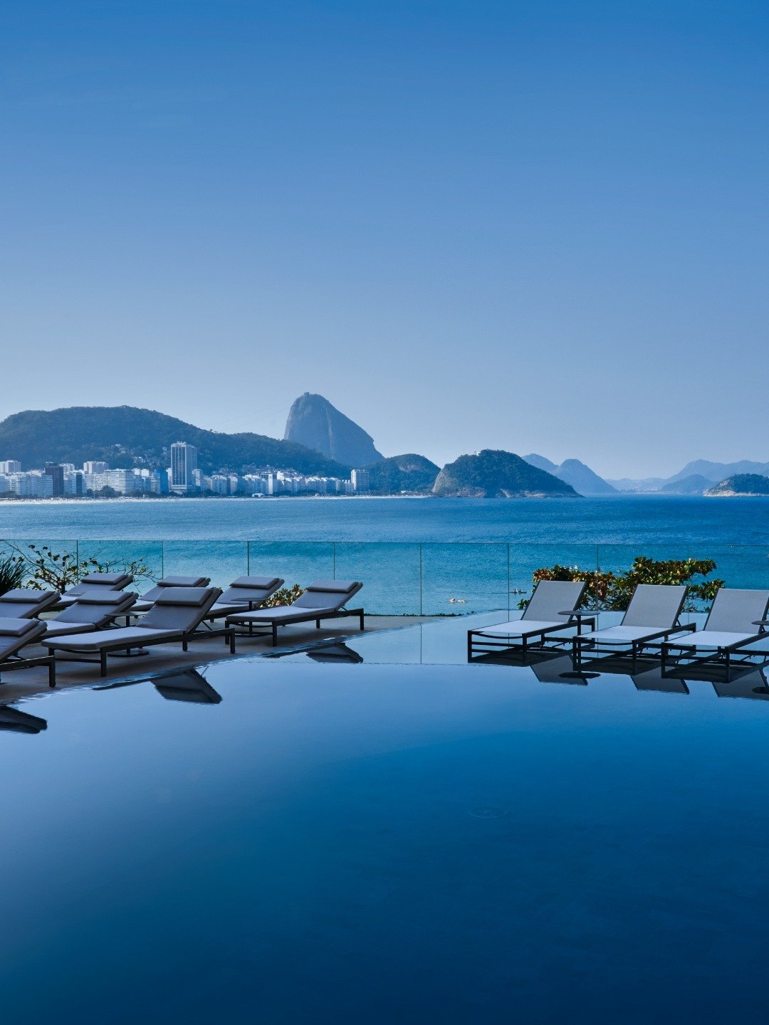 Guia do verão brasileiro destaca o cenário azul vibrante da piscina com espreguiçadeiras minimalistas e vista para o mar