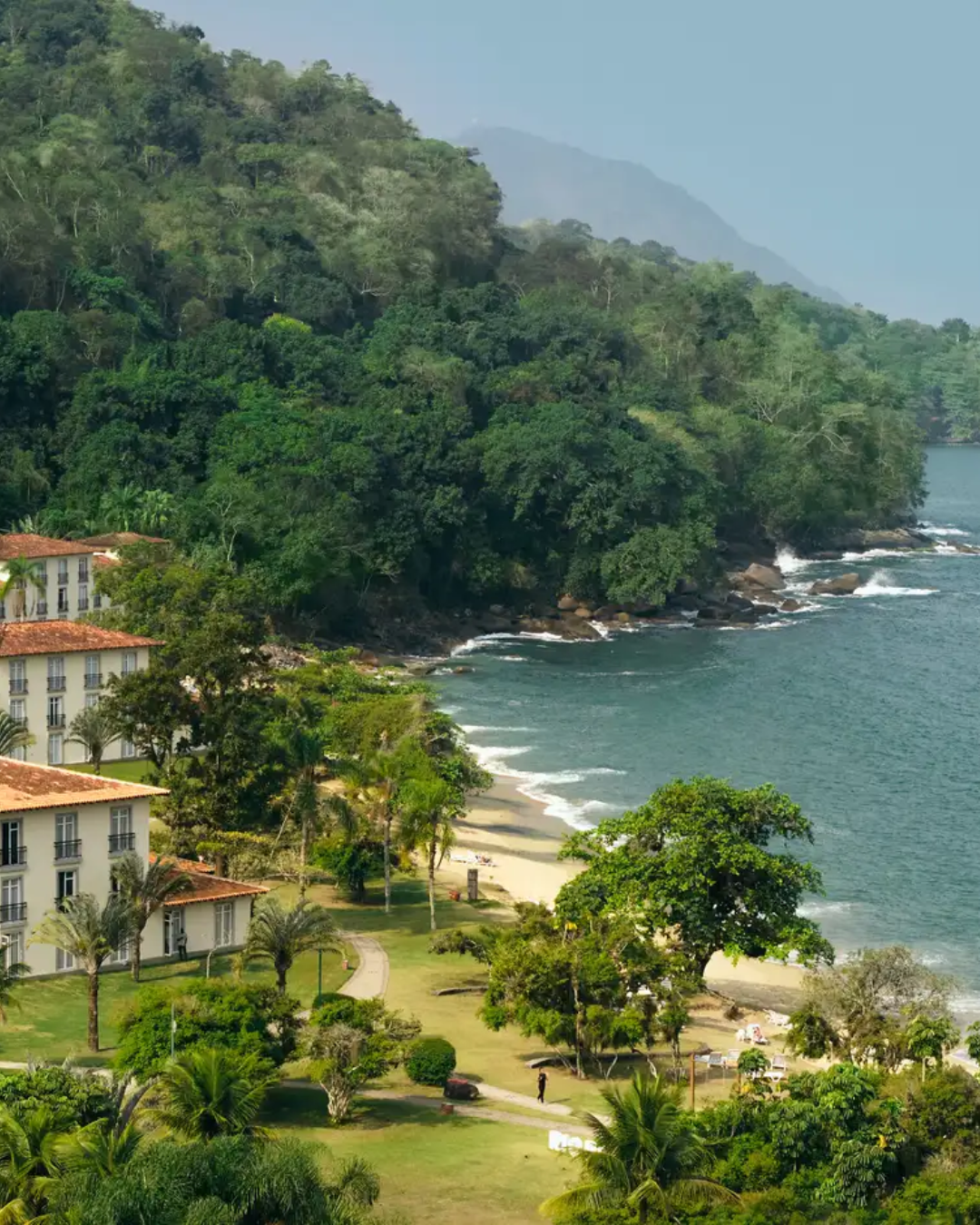 Paisagem litorânea com verde intenso, mar azul e céu claro, cenário ideal para o guia do verão brasileiro.