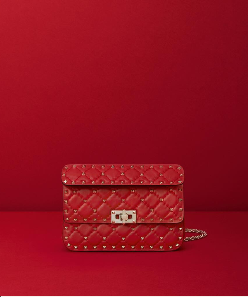 Bolsa Valentino vermelha em couro matelassê com tachas douradas e fecho metálico, exibindo luxo e ousadia.