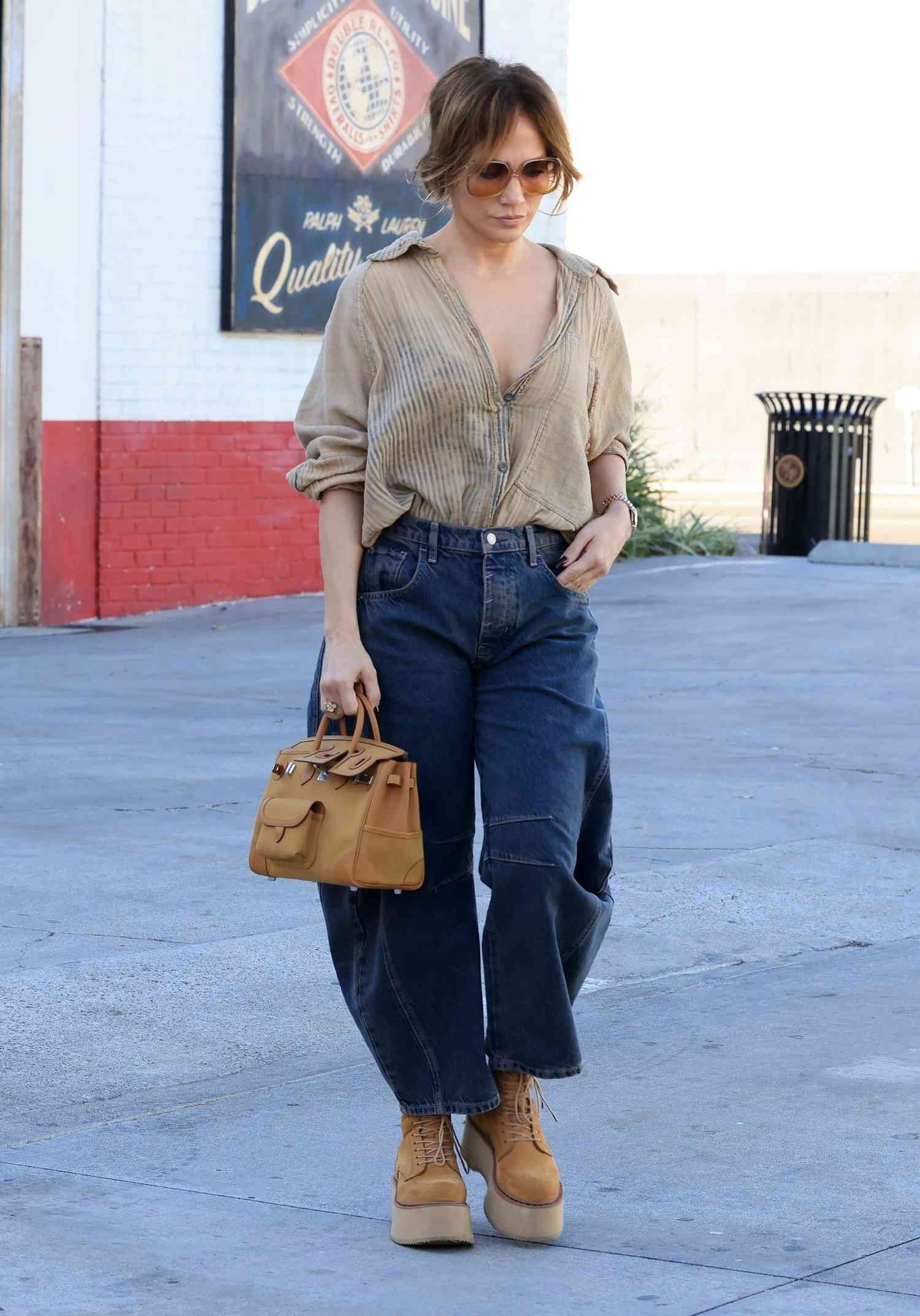 Modelo caminha com postura confiante usando calça barrel jeans azul escuro de modelagem ampla, camisa bege de tecido leve e