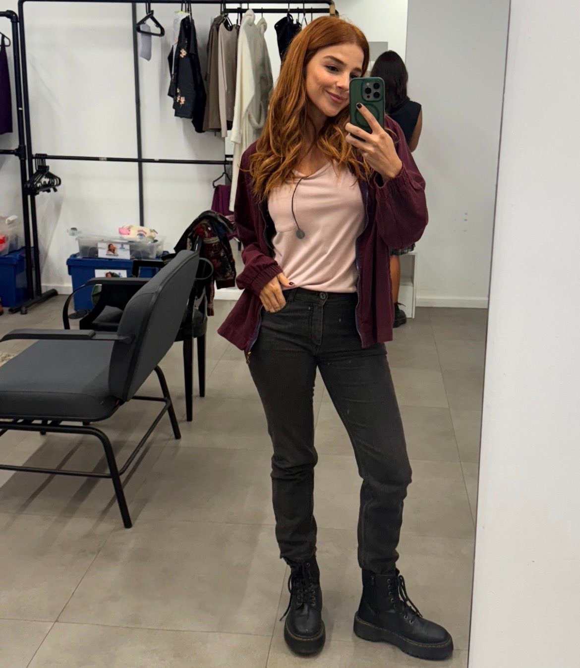 Lorena e Juquinha posam com jaqueta vinho de tecido leve, camiseta rosa clara, calça preta justa e botas pretas robustas, em