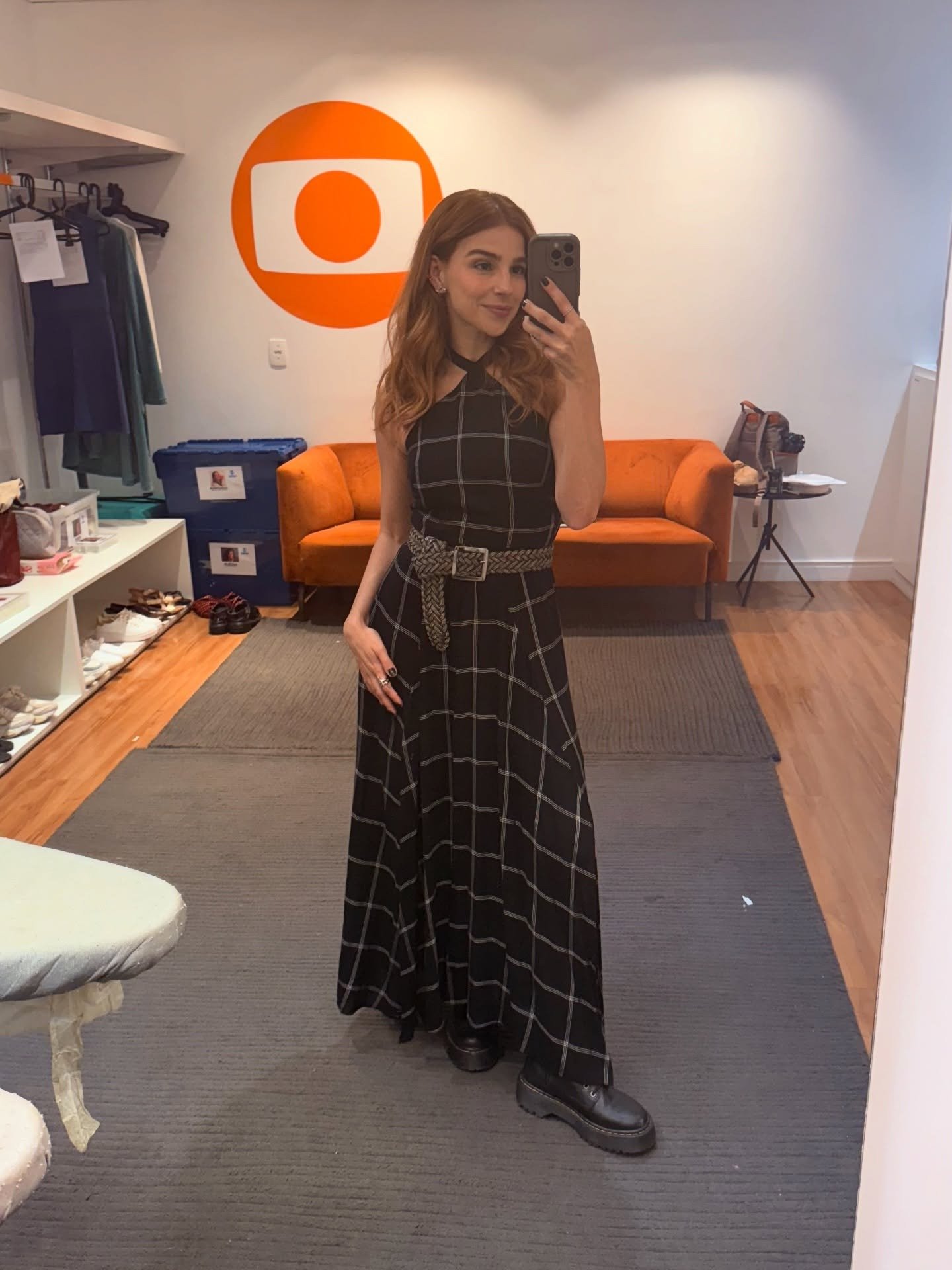 Lorena e Juquinha posam com vestido longo preto xadrez de modelagem fluida, cinto trançado e botas pretas, em ambiente