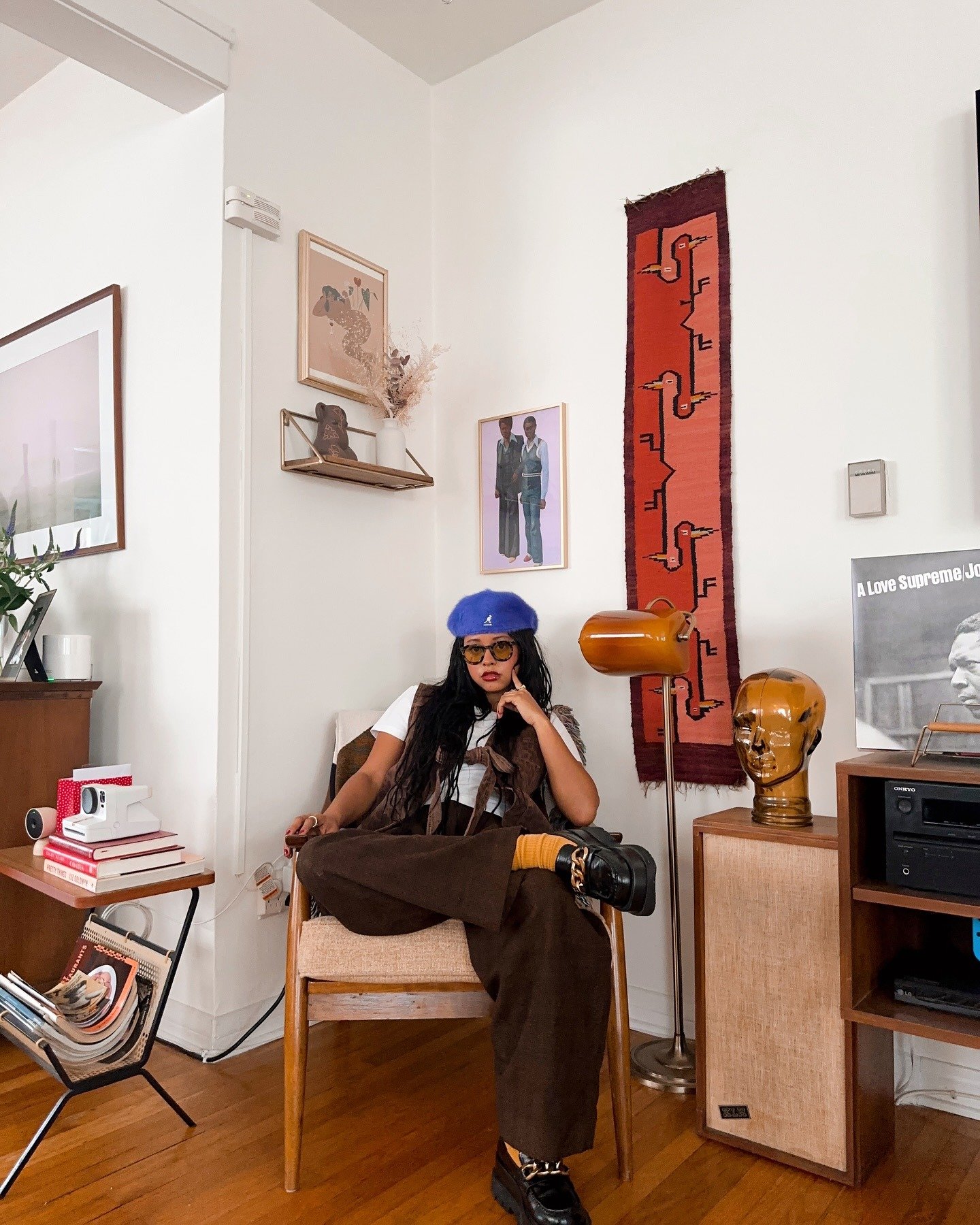 Modelo senta com postura confiante usando boina Kangol azul vibrante de lã, calça e colete marrons em veludo, camiseta