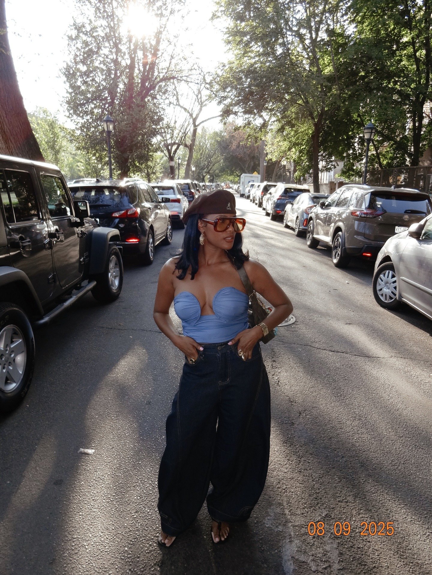 Modelo posa confiante na rua com boina kangol marrom de lã, top azul estruturado e calça jeans larga, em luz dourada suave.