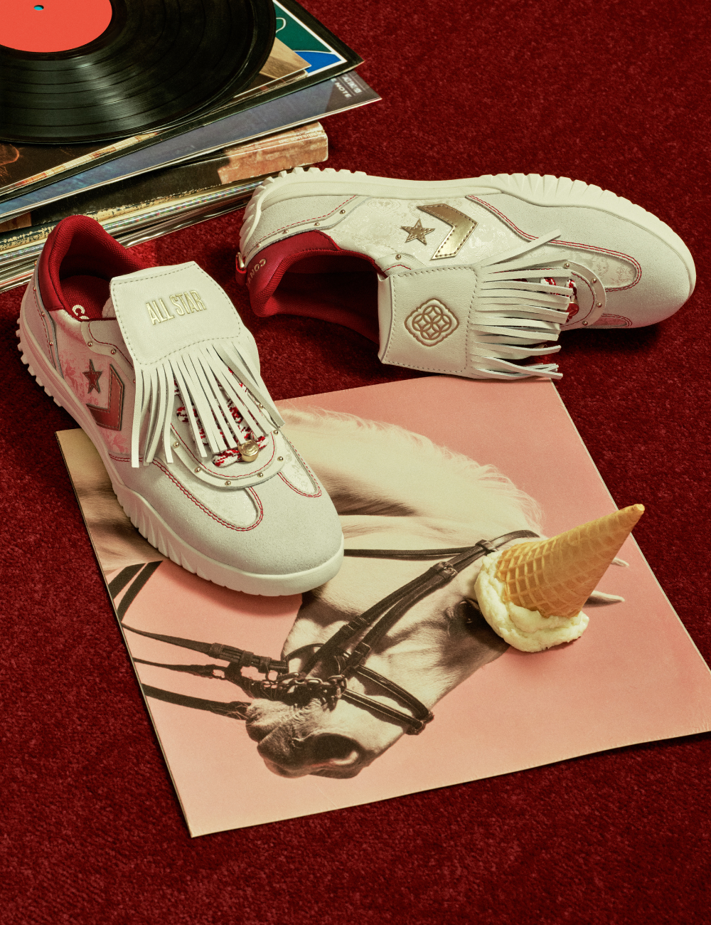 Tênis branco com franjas e detalhes vermelhos em camurça, sobre capa de disco com cavalo, evocando o Zodíaco Chinês.