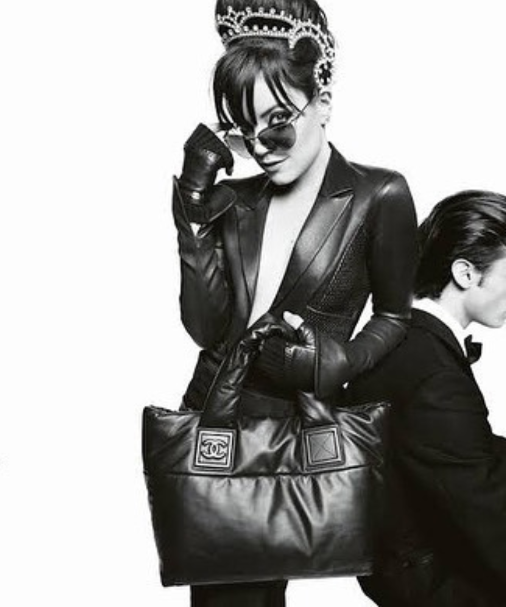 Lily Allen posa com jaqueta e luvas de couro preto, óculos escuros e tiara de pérolas, segurando bolsa Chanel com atitude