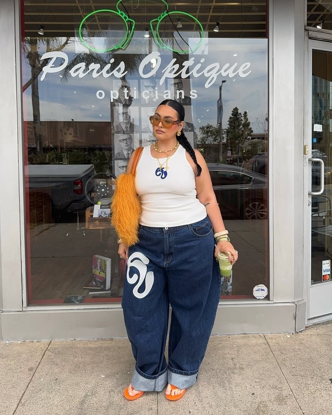 Look com calça jeans ampla de lavagem escura e regata branca justa com estampa azul, combinados com acessórios dourados e