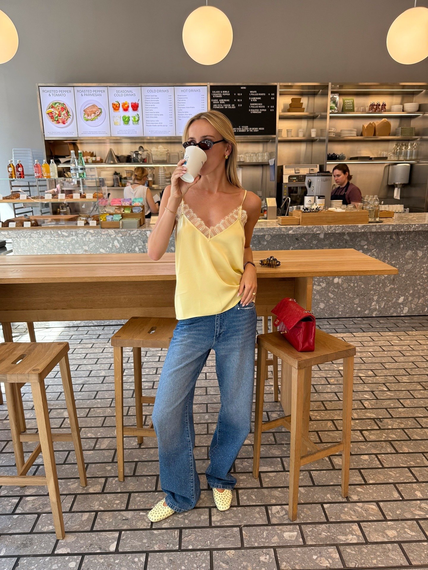 Modelo posa casual com calça jeans reta azul e regata amarela de tecido leve com renda, criando look fresco e sofisticado.