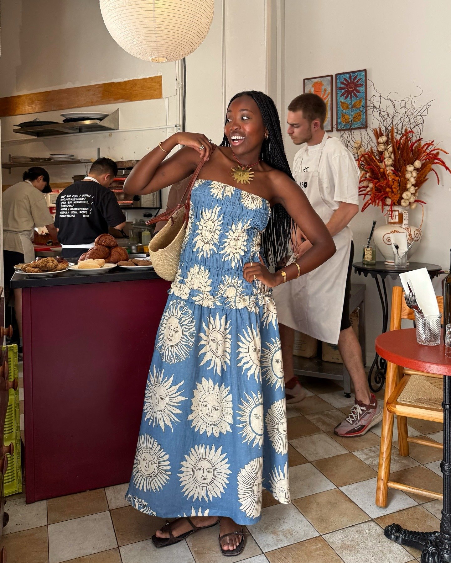 Modelo sorri e posa com vestido longo azul de algodão com estampa de sóis brancos, sandálias rasteiras e bolsa de palha,