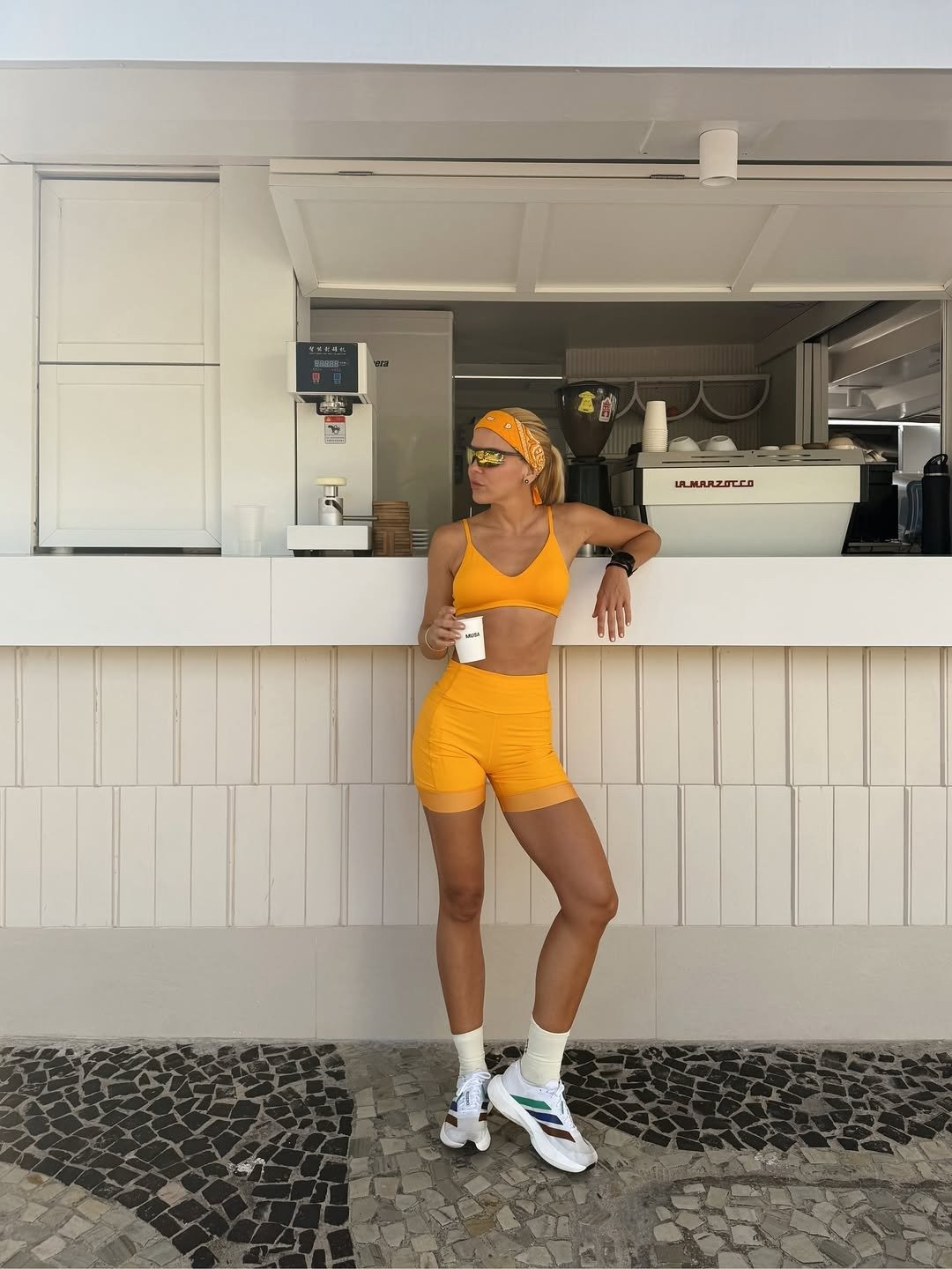 Look para academia feminino com top e shorts justos em tecido tecnológico laranja vibrante, combinados com bandana e tênis