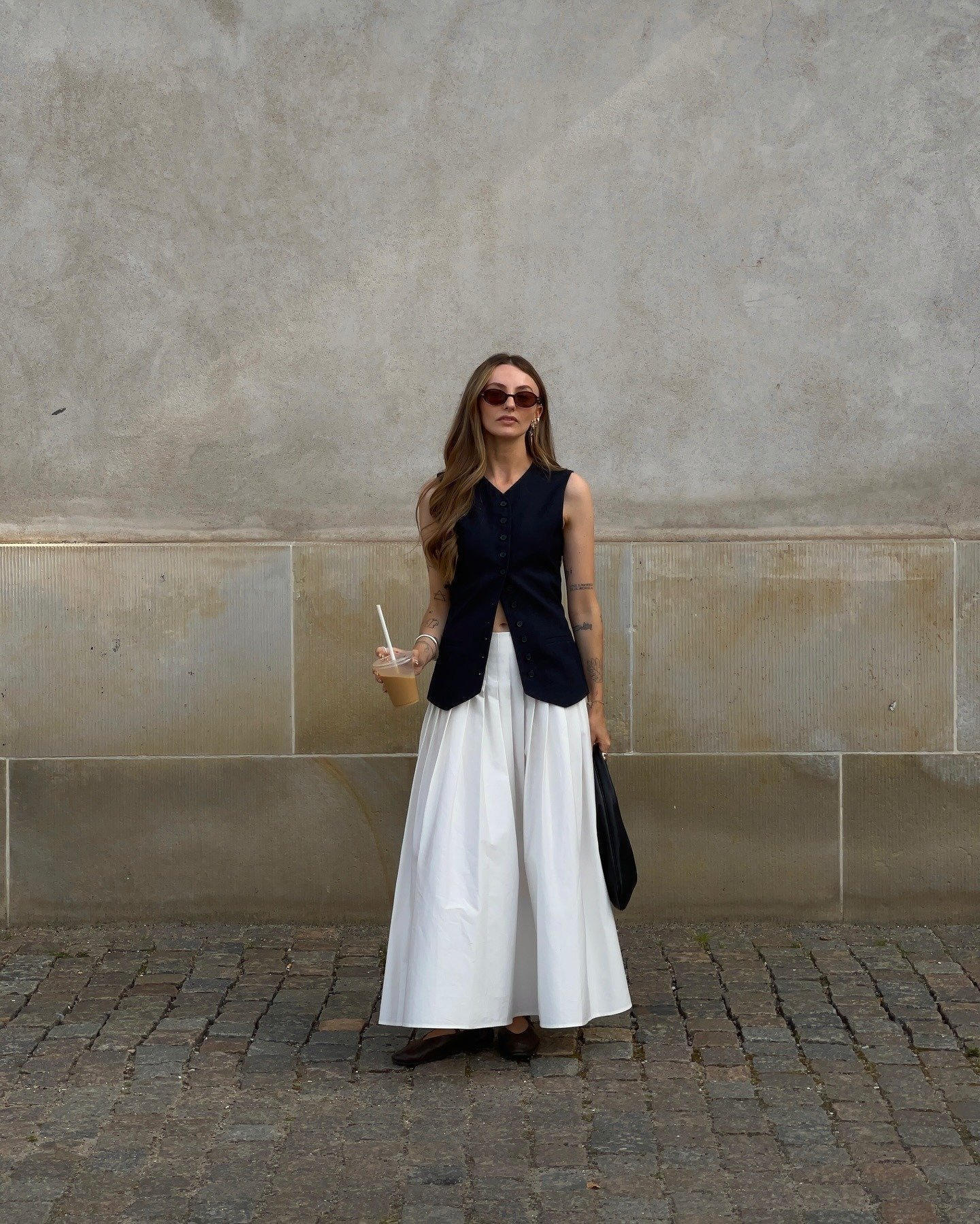 Modelo posa com looks fáceis e estilosos usando colete preto acinturado, saia ampla branca de tecido estruturado e