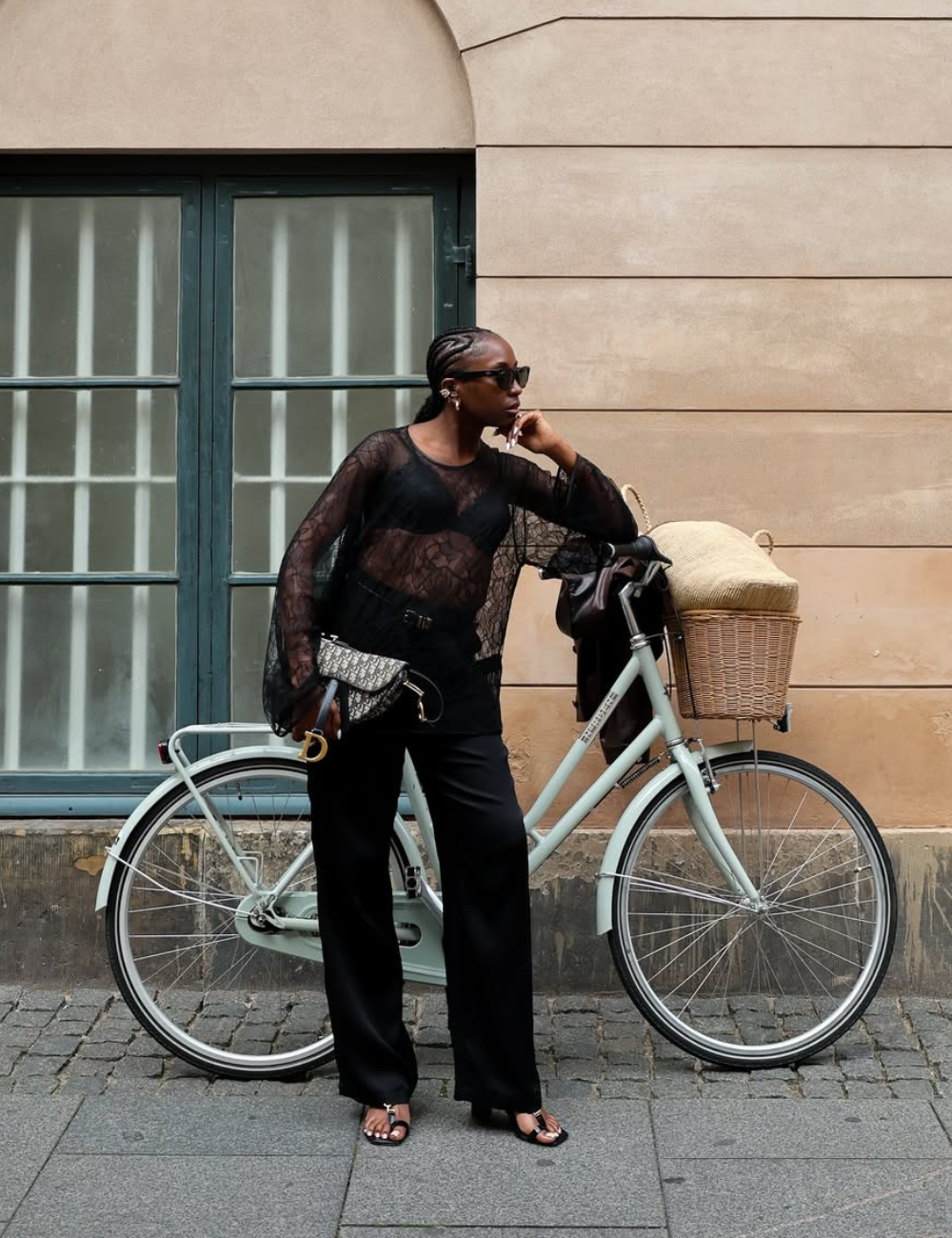 Modelo posa com postura confiante usando blusa preta transparente de renda, calça ampla e acessórios sofisticados.