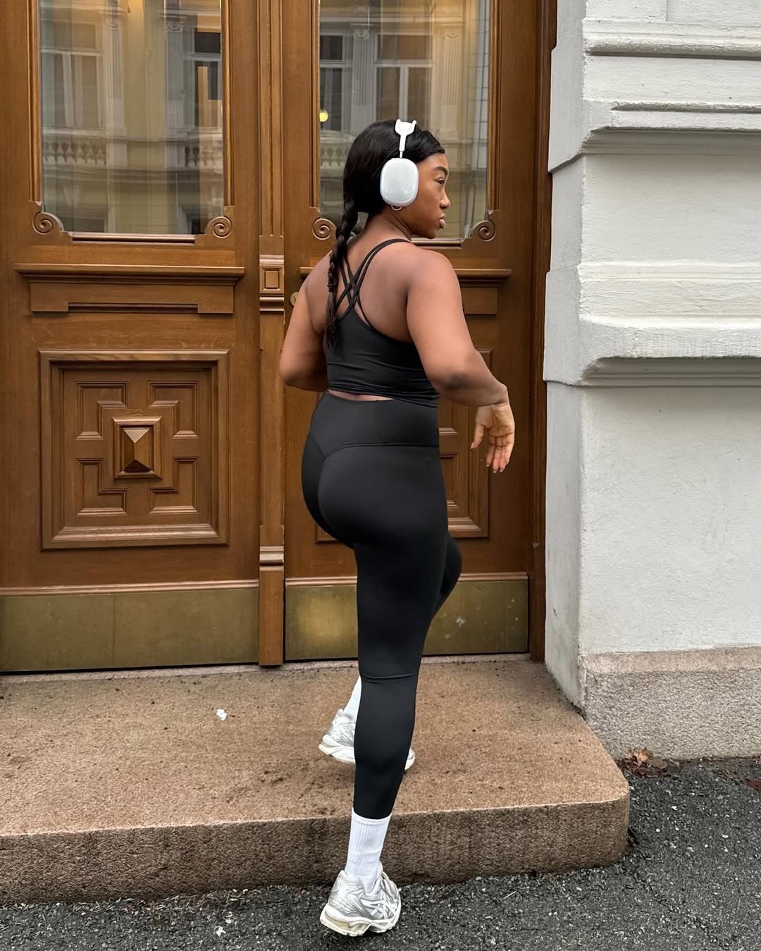 Modelo posa de costas com look para academia feminino em preto, top cropped com alças cruzadas e legging justa, combinando